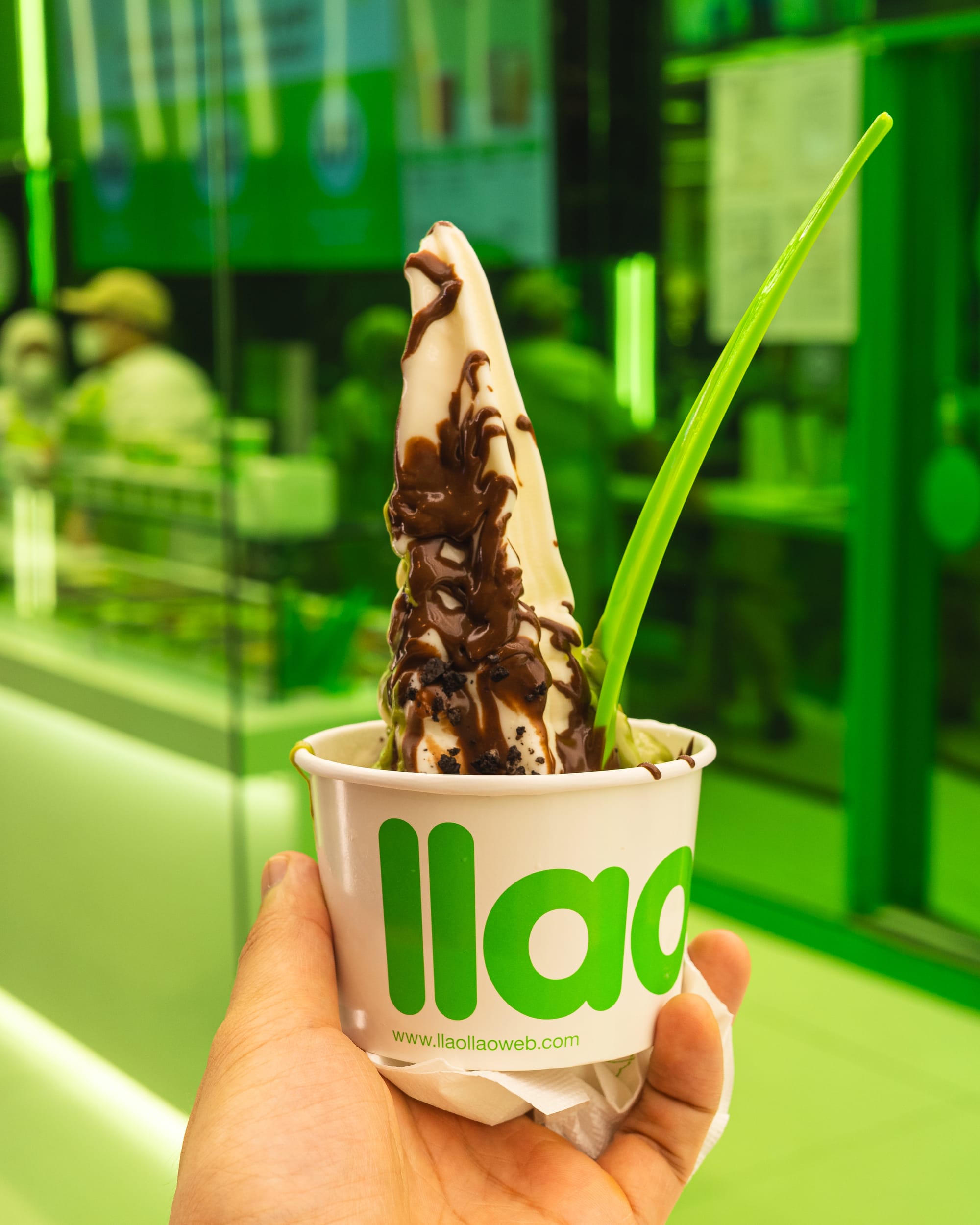 Hand holding a tub of frozen yoghurt with chocolate sauce