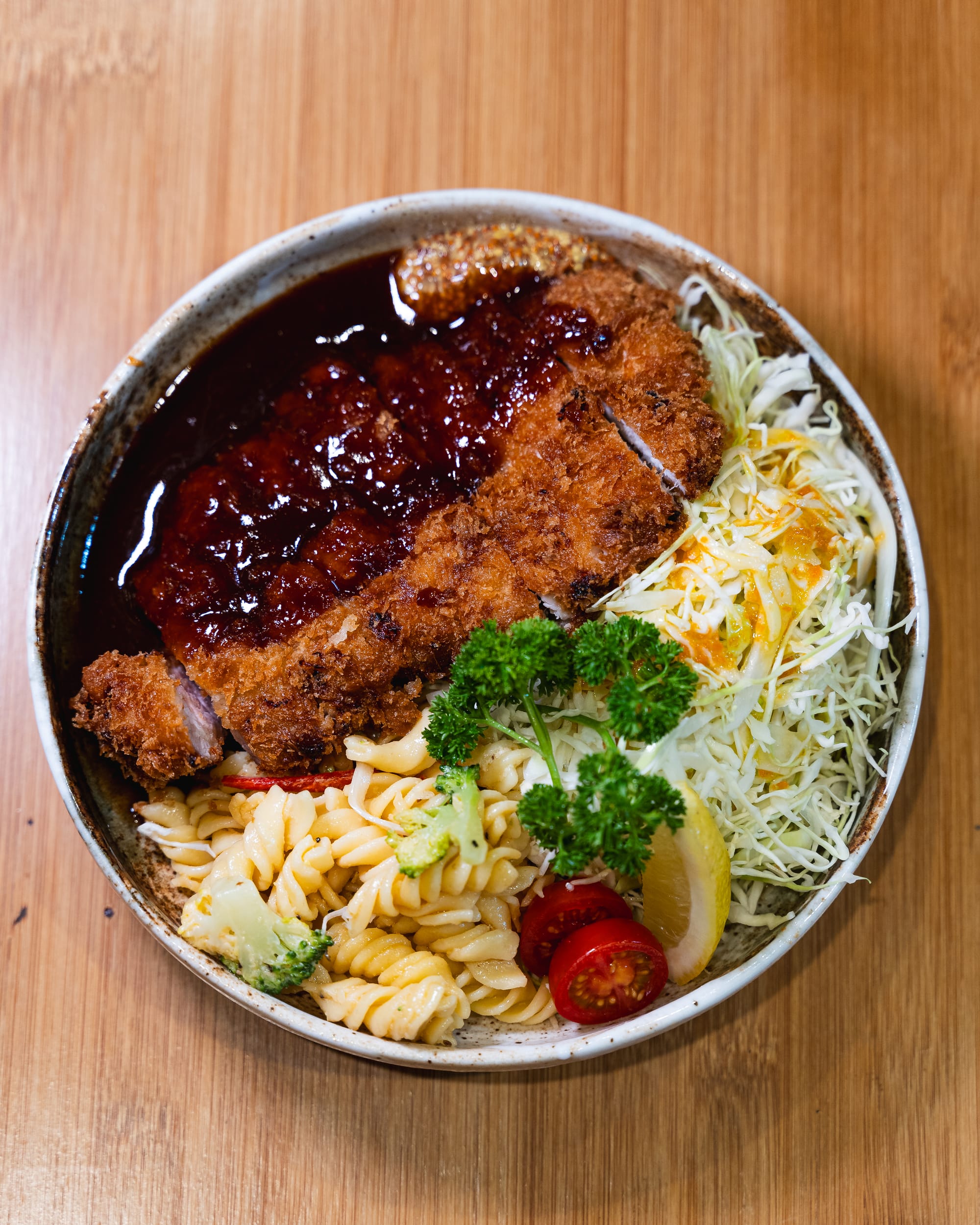 Top down shot of tonkatsu with sauce, pasta salad and raddish