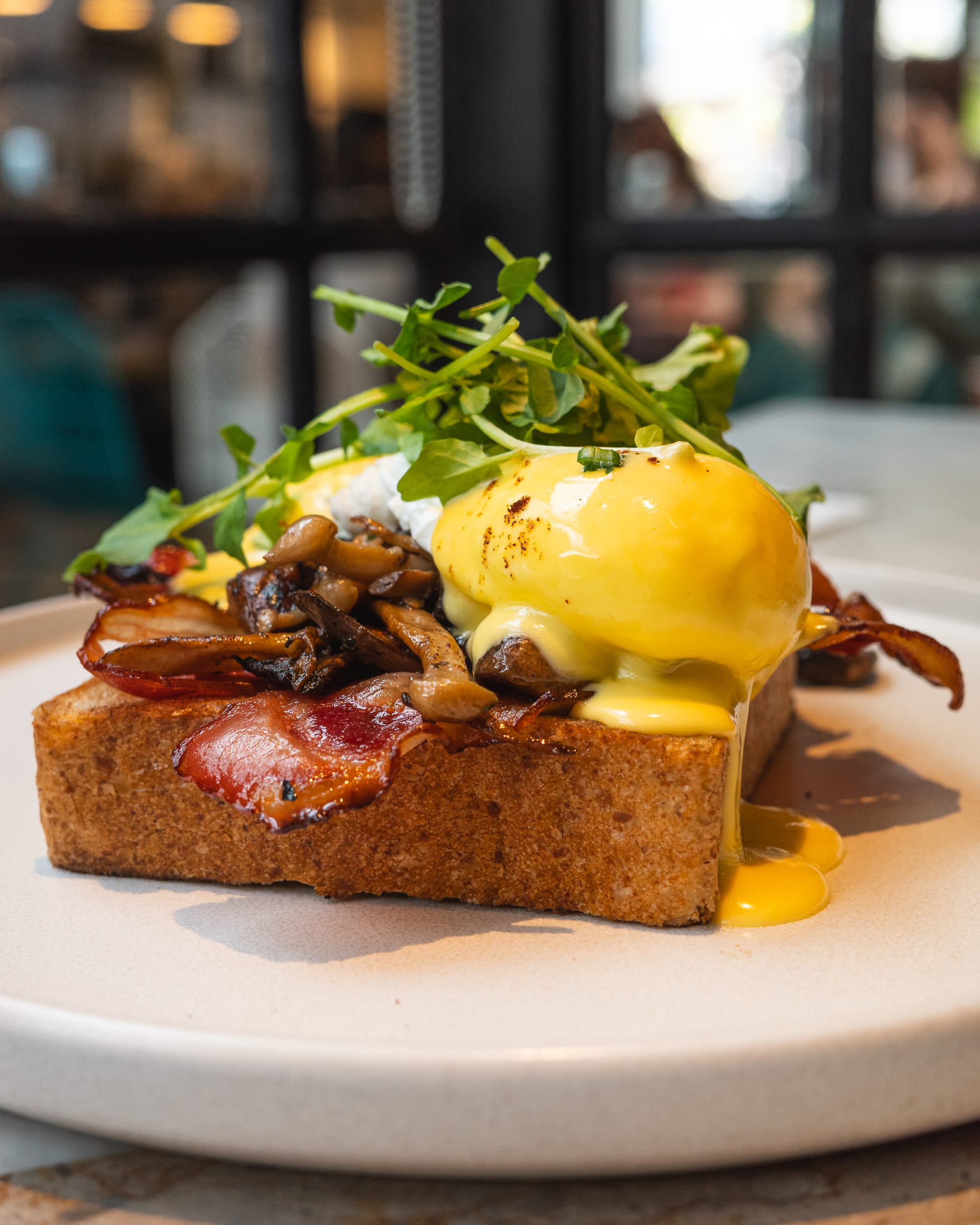 Eggs benedict on toast with bacon and greens