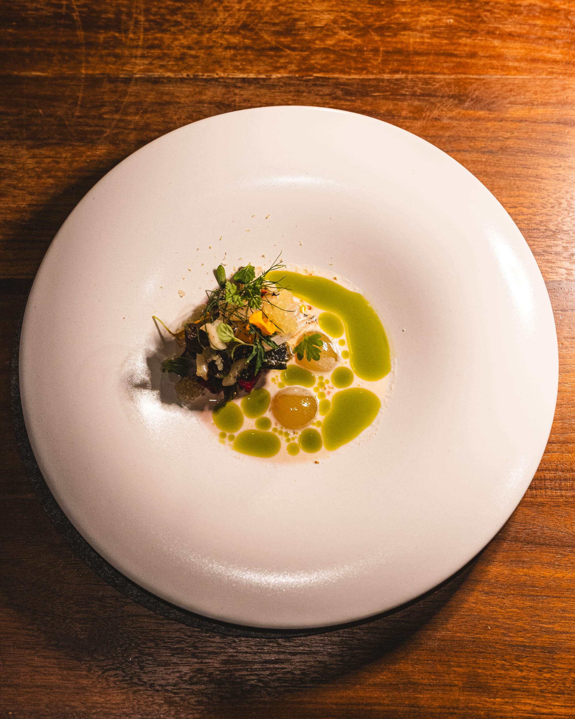 Top down shot of squid topped with various microgreens and ikura, served with macadamia milk sauce