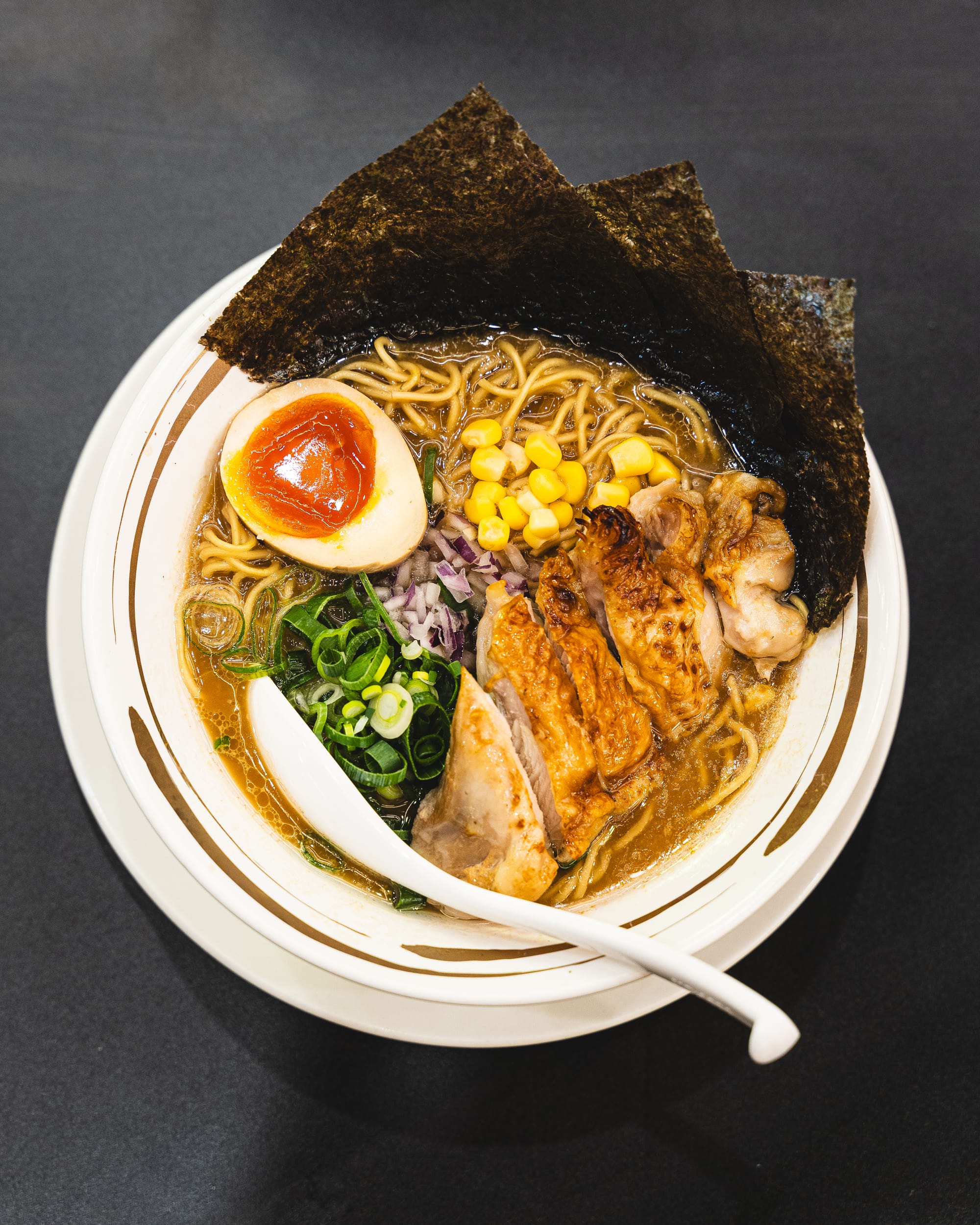 Top down shot of ramen with noodles, chicken, spring onions, egg, corn and seaweed