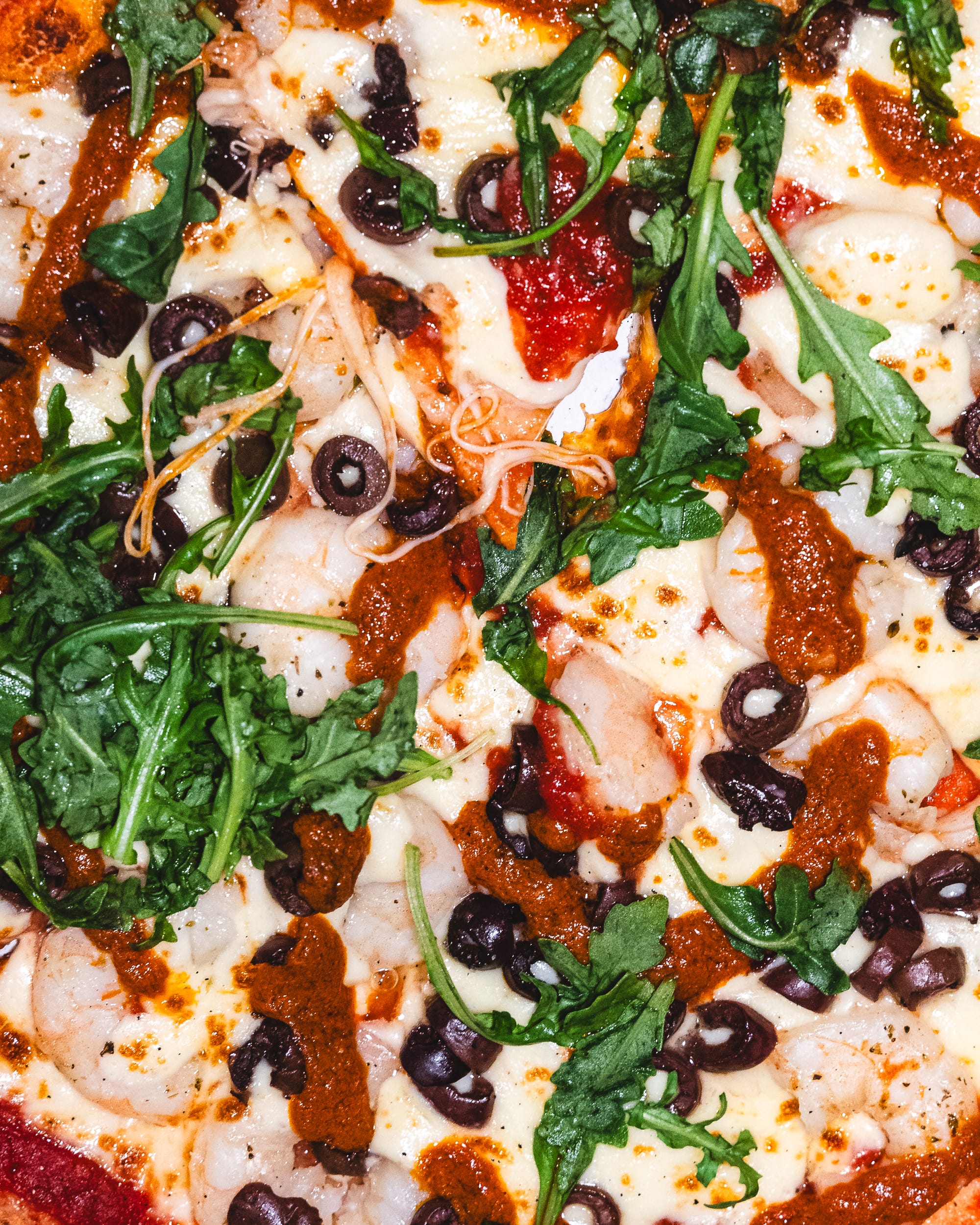 Top down shot of pizza with rocket, cheese, prawns and olives