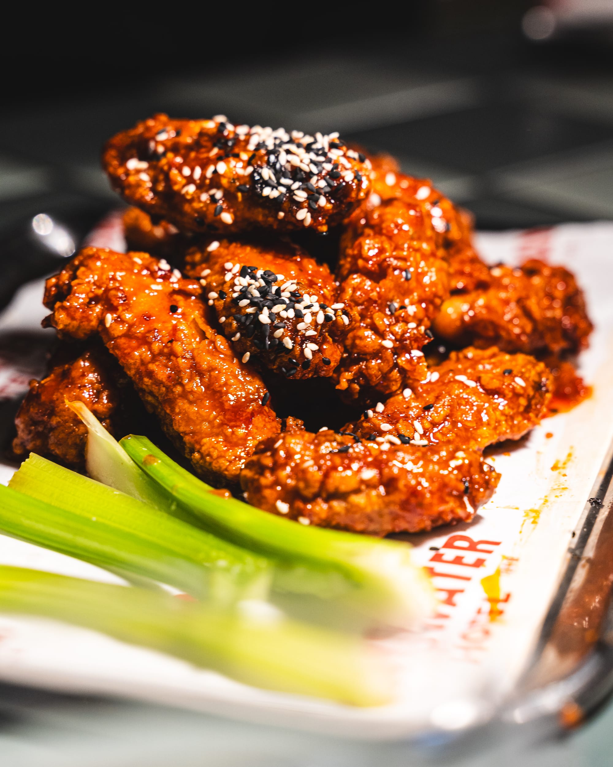 Close up of fried chicken wings topped with sesame seeds and served with a side of celery