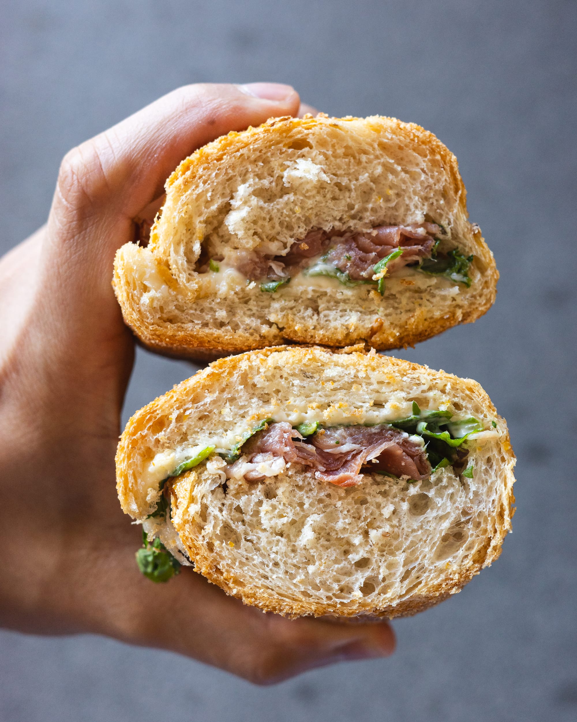 Hand holding two Italian sandwiches showing the cut cross area