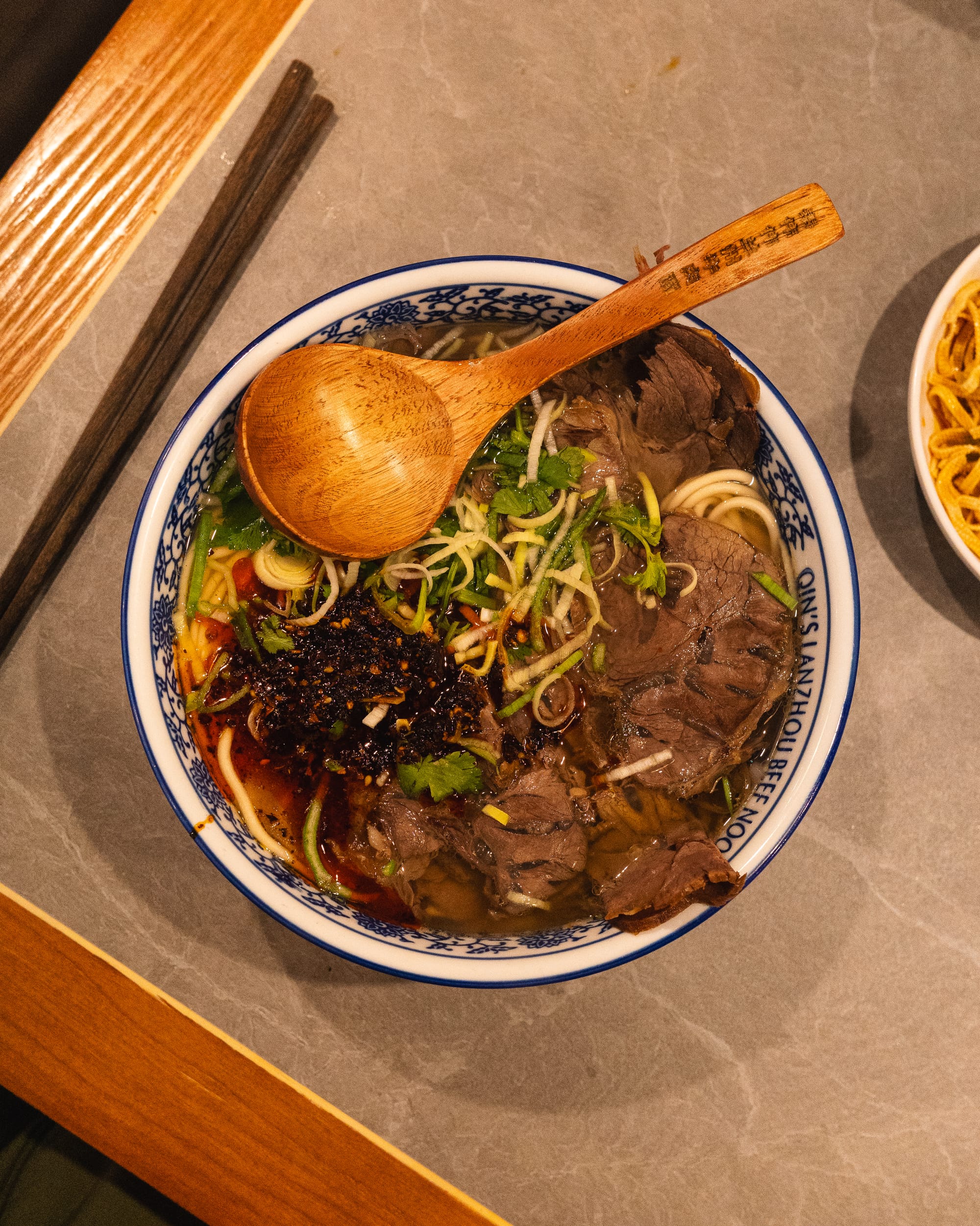 Top down shot of noodles with sliced beef, chilli crunch and spring onions