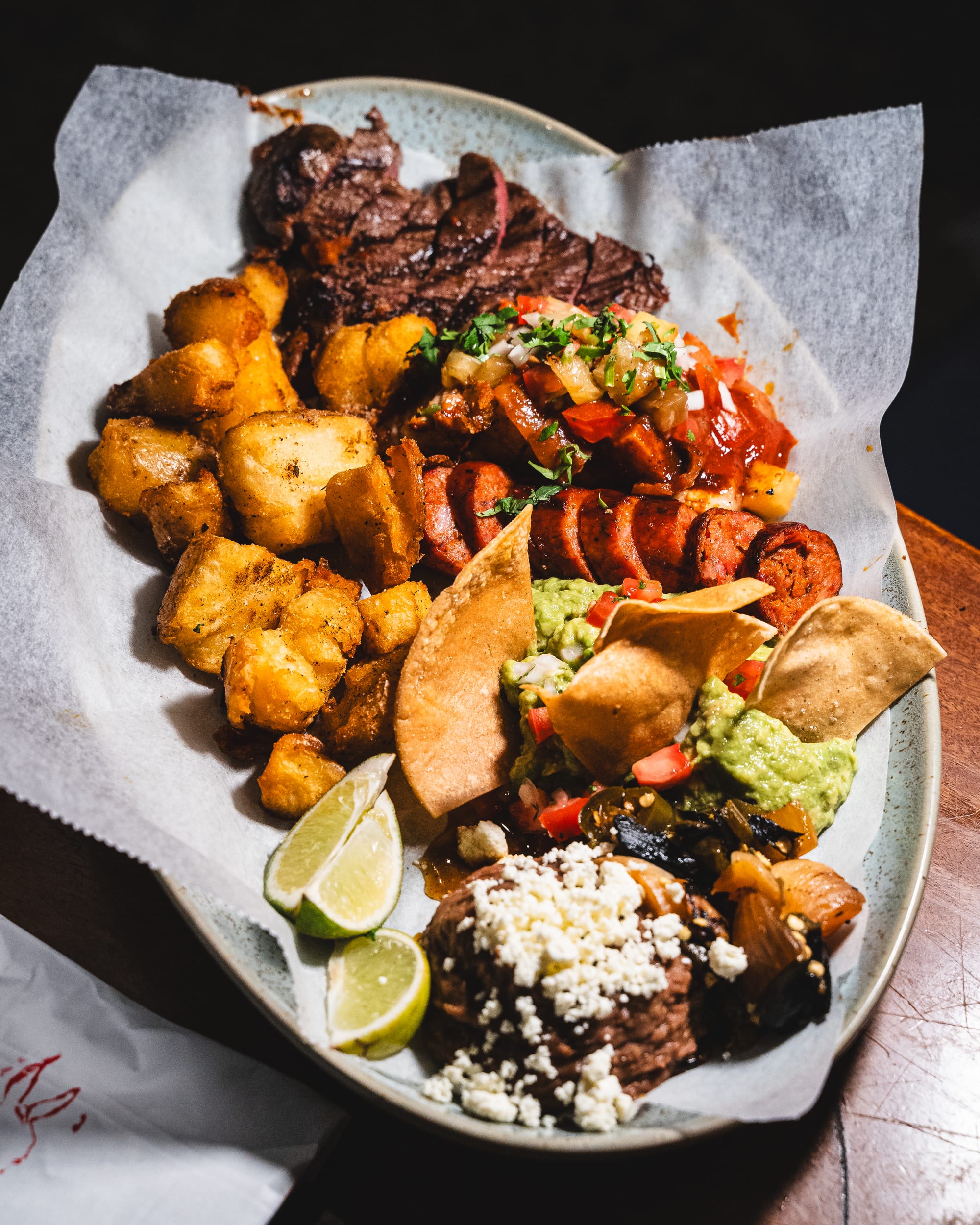 Plate of carne asada with streak, beans, potato, chorizo, guac and corn chips