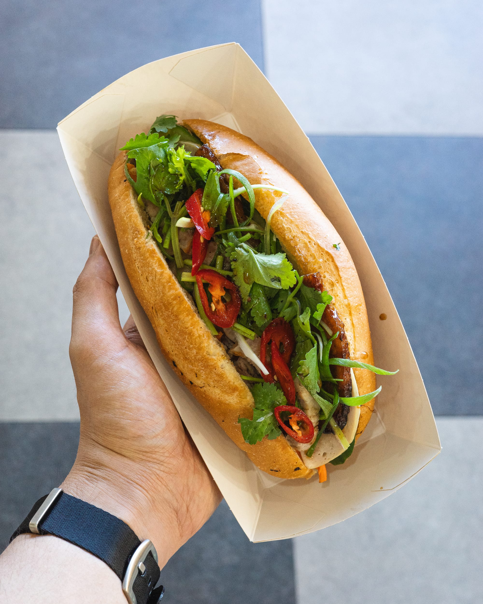 Close up of hand holding banh mi with chilli and coriander showing