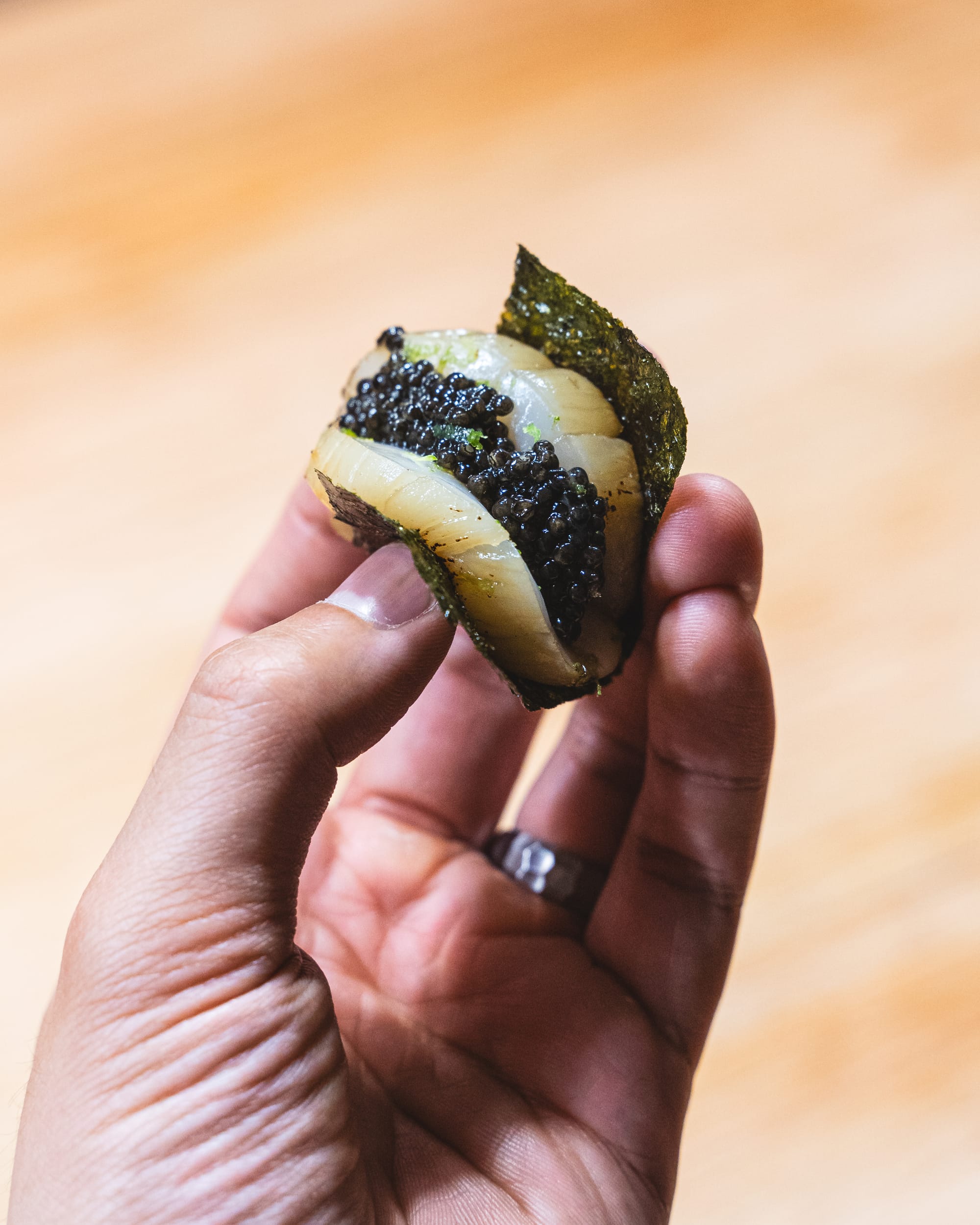 Close up of hand holding scallop with caviar placed on top