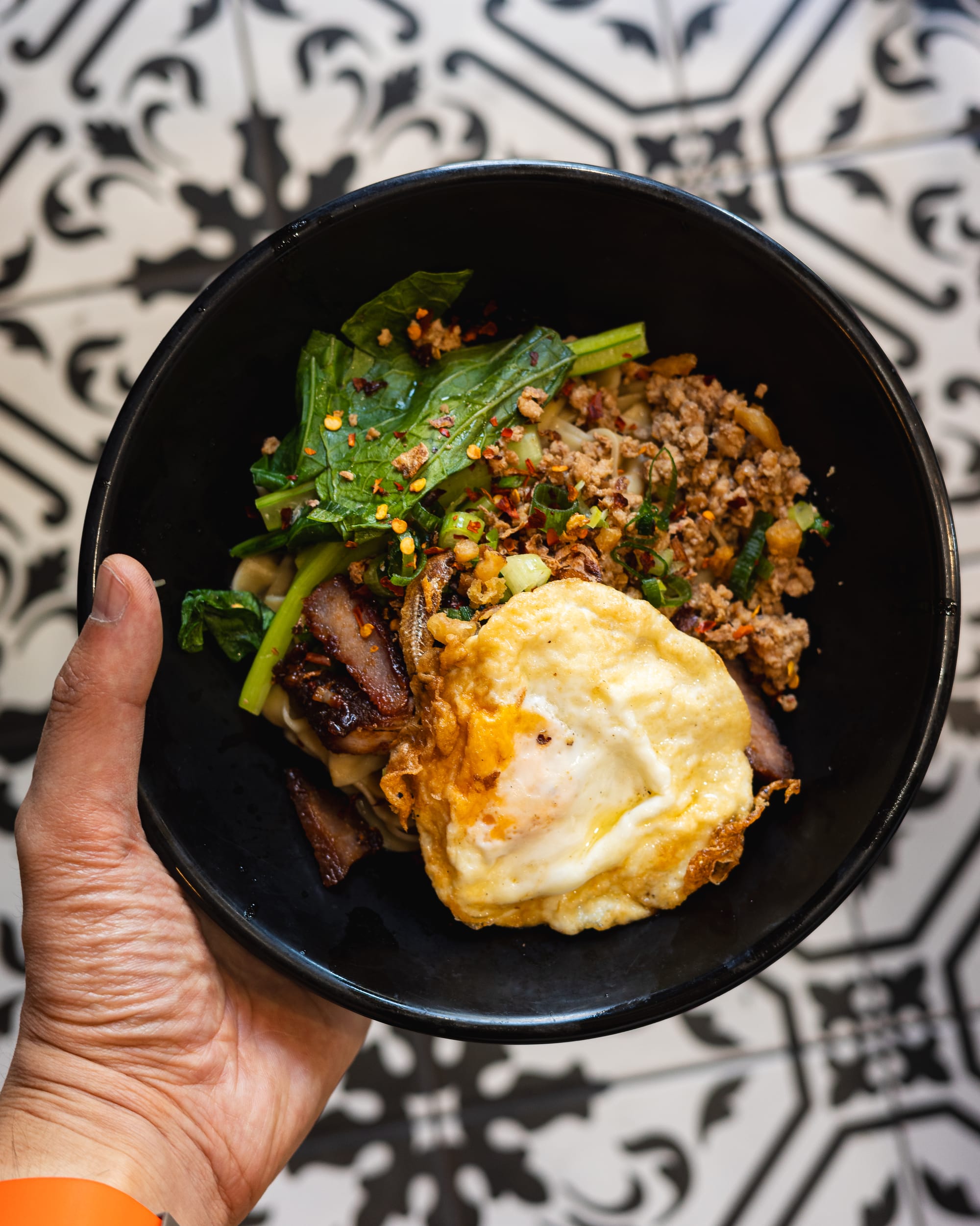 Top down shot of hand holding a bowl of noodles with mince beef, egg and vegetables