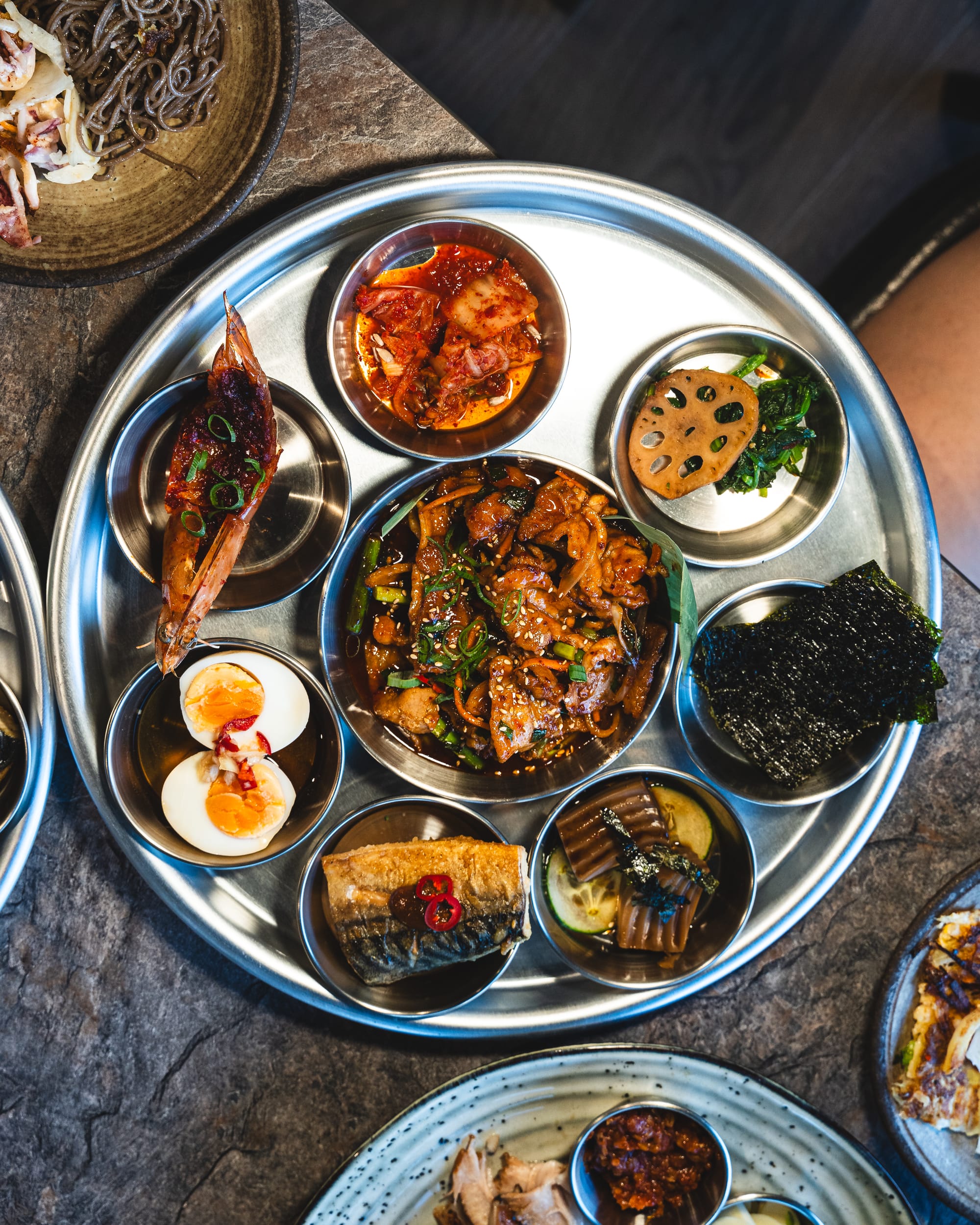 Top down shot of stainless steel plate with Korean dishes in smaller stainless steel plate