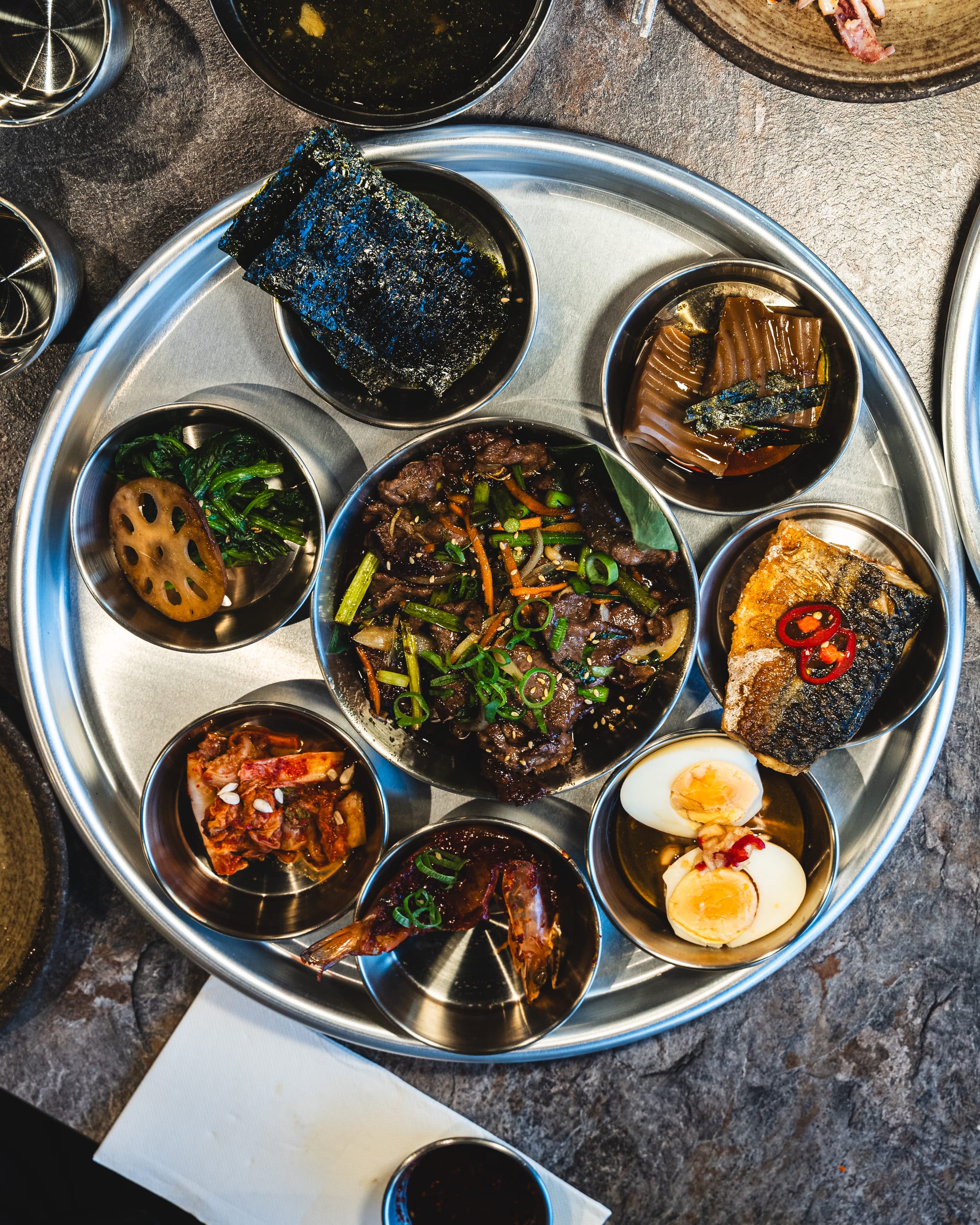 Top down shot of stainless steel plate with Korean dishes in smaller stainless steel plate