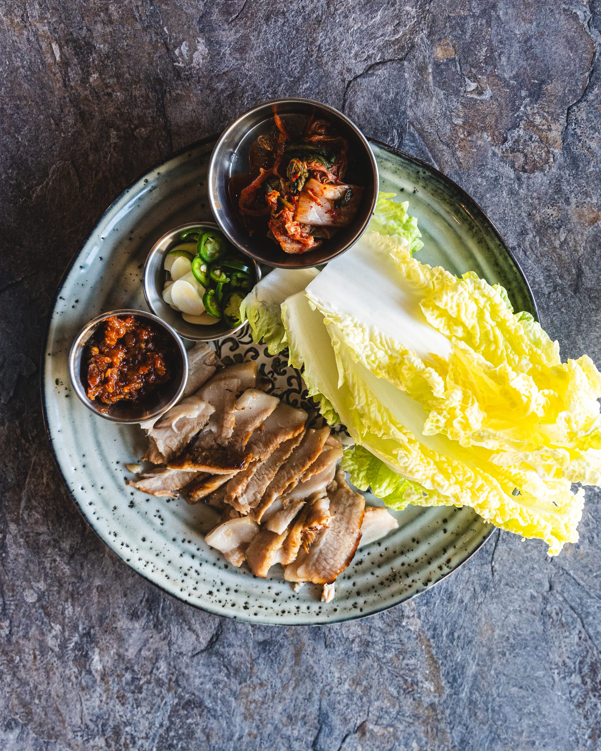 Top down shot of pork jowl, lettuce and side condiments