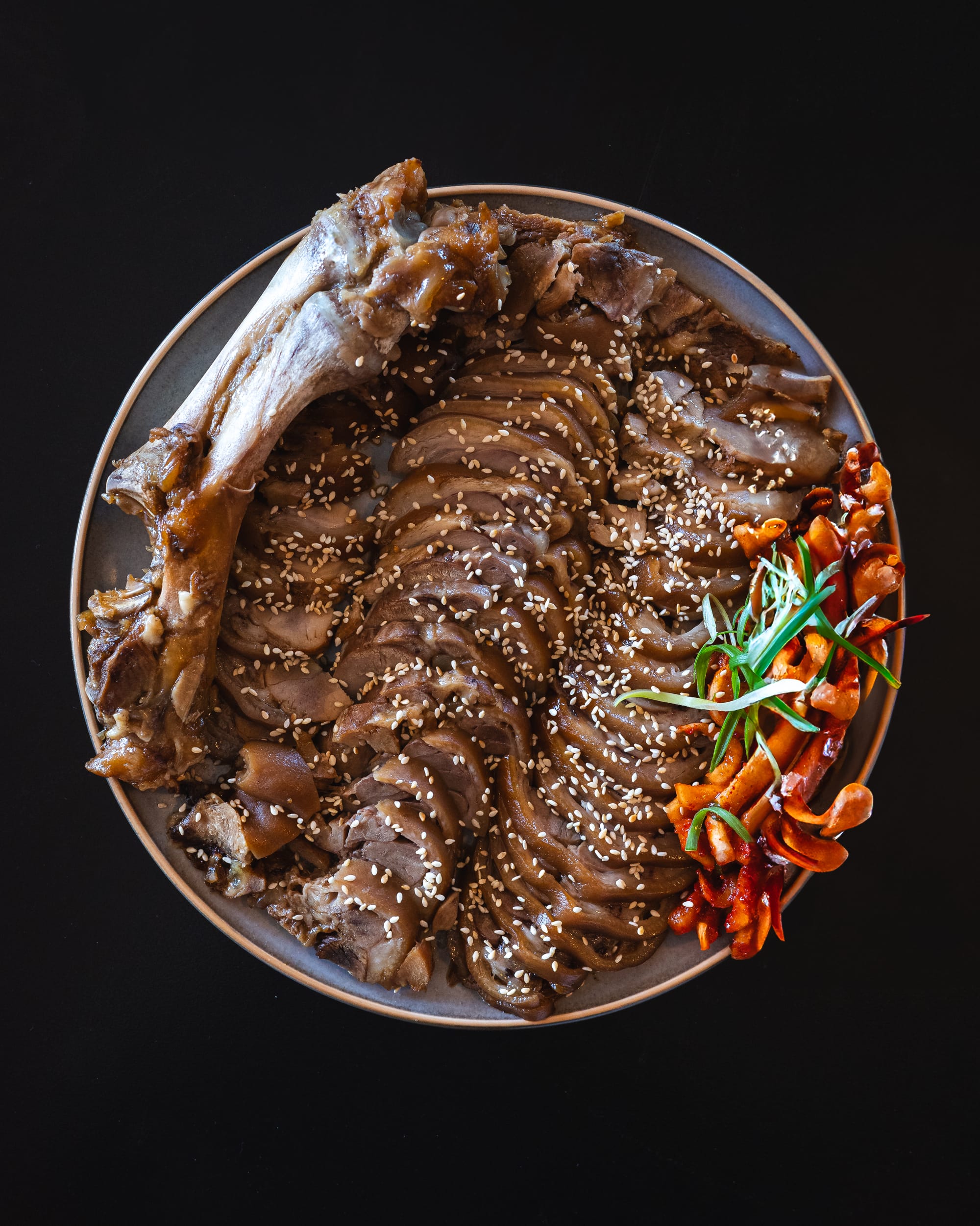 A plate of sliced beef topped with sesame seeds and garnished with green onions and kimchi.