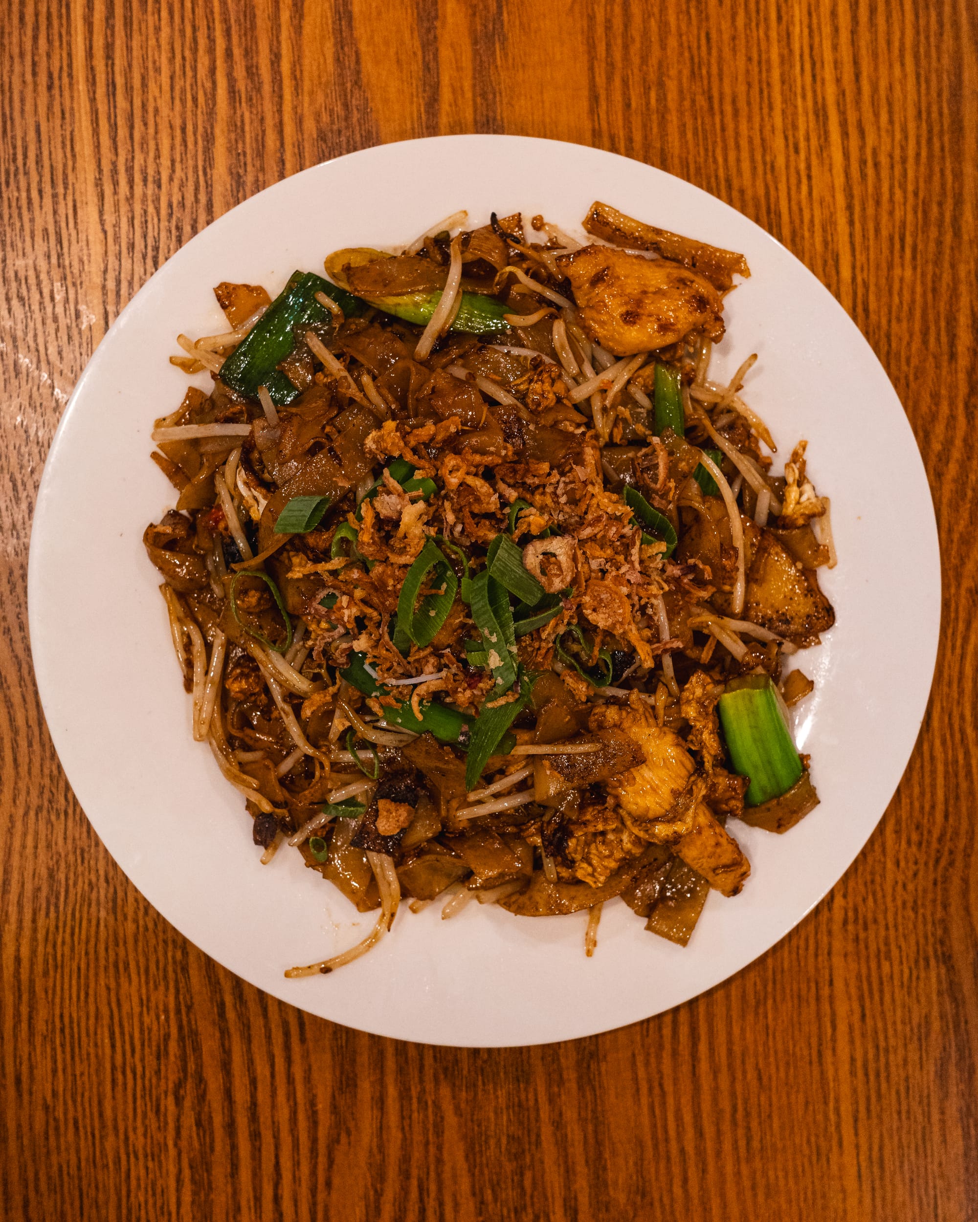 A plate of stir-fried flat noodles with vegetables and a sprinkle of fried shallots.