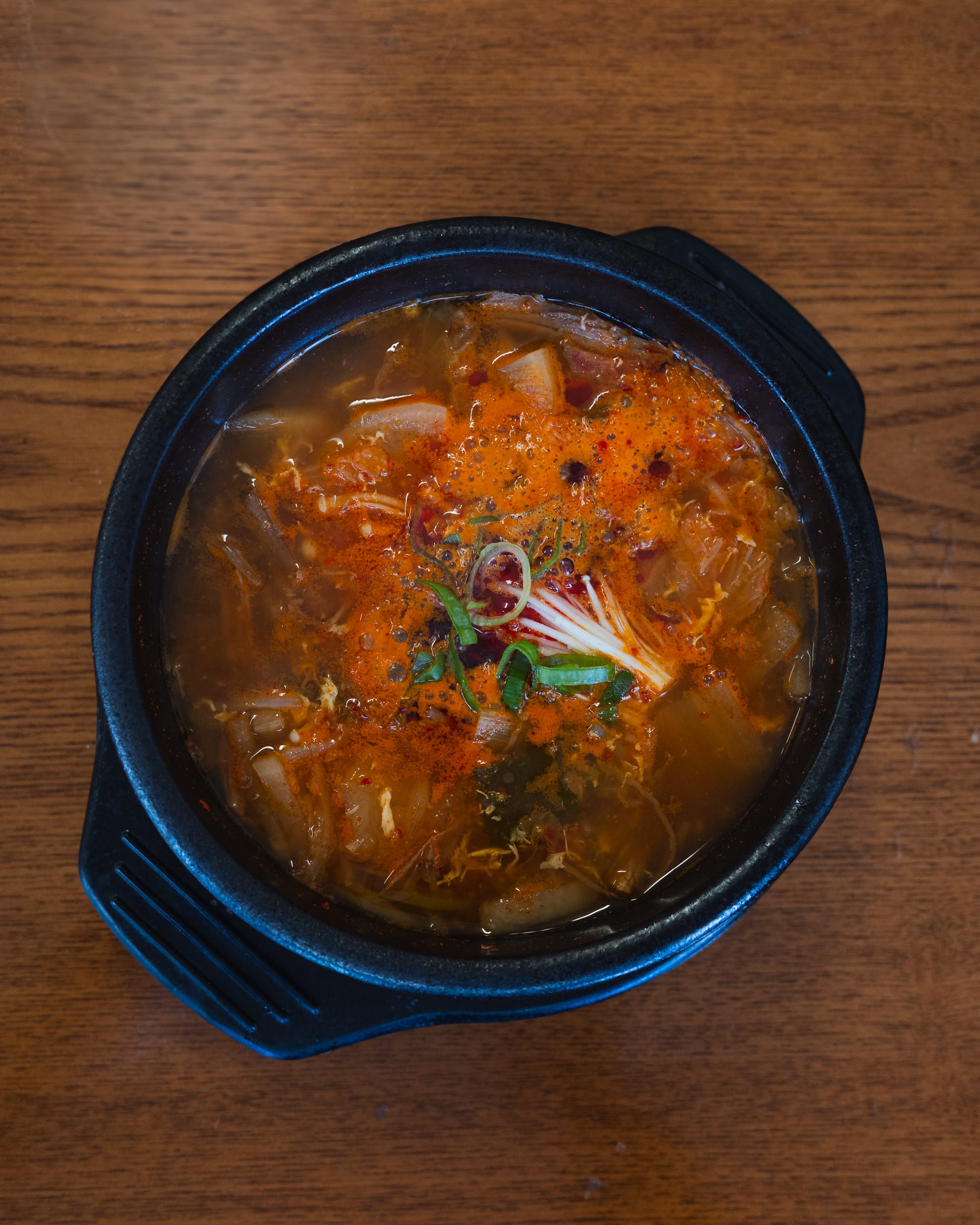 A small black bowl of spicy kimchi stew garnished with microgreens.