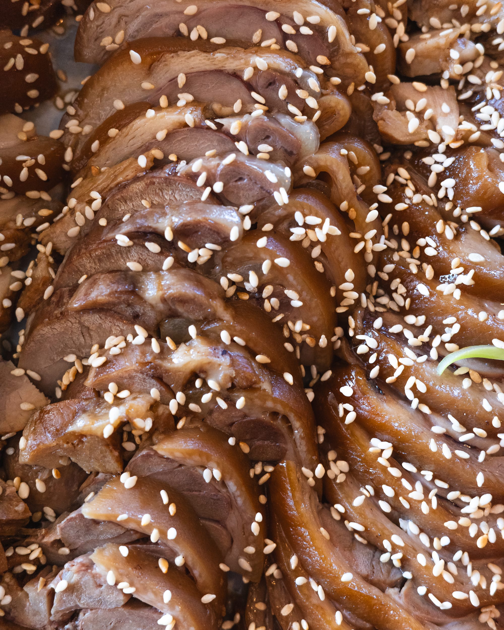 Close-up of thinly sliced pork belly garnished with sesame seeds.