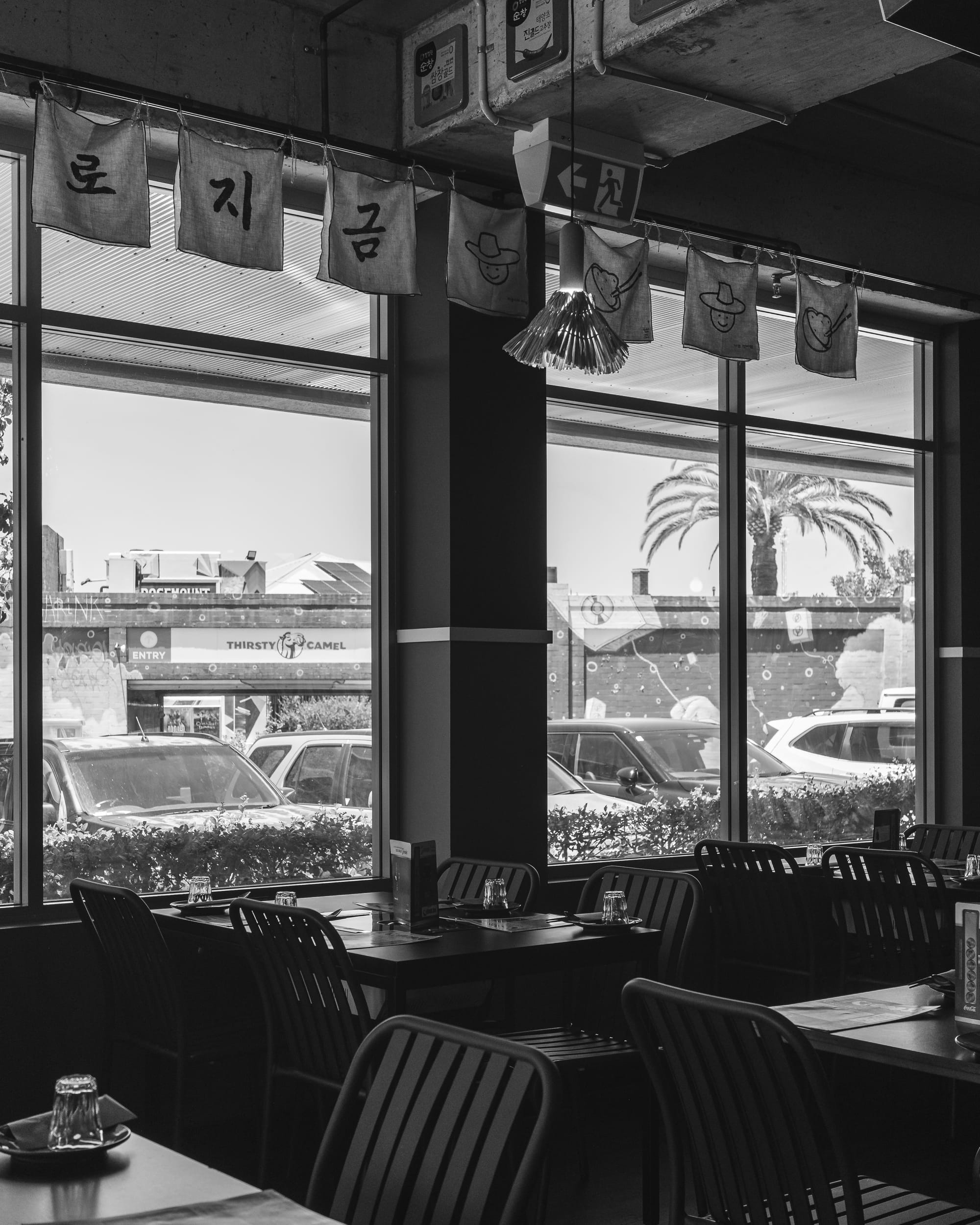 Black and white image of a restaurant interior with a view of the street through large windows.