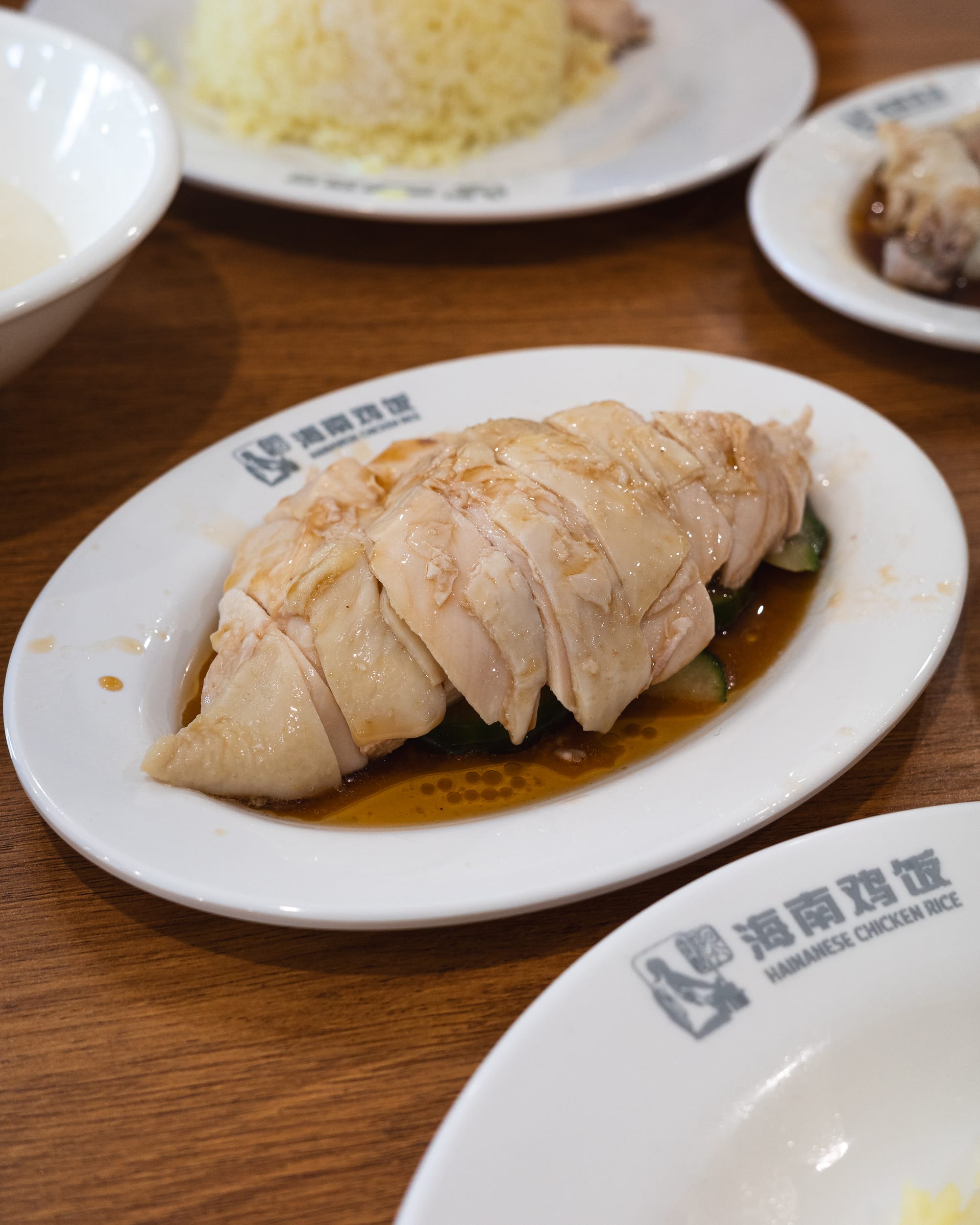 Steamed chicken breast on a plate with soy-based sauce, accompanied by rice in the background.