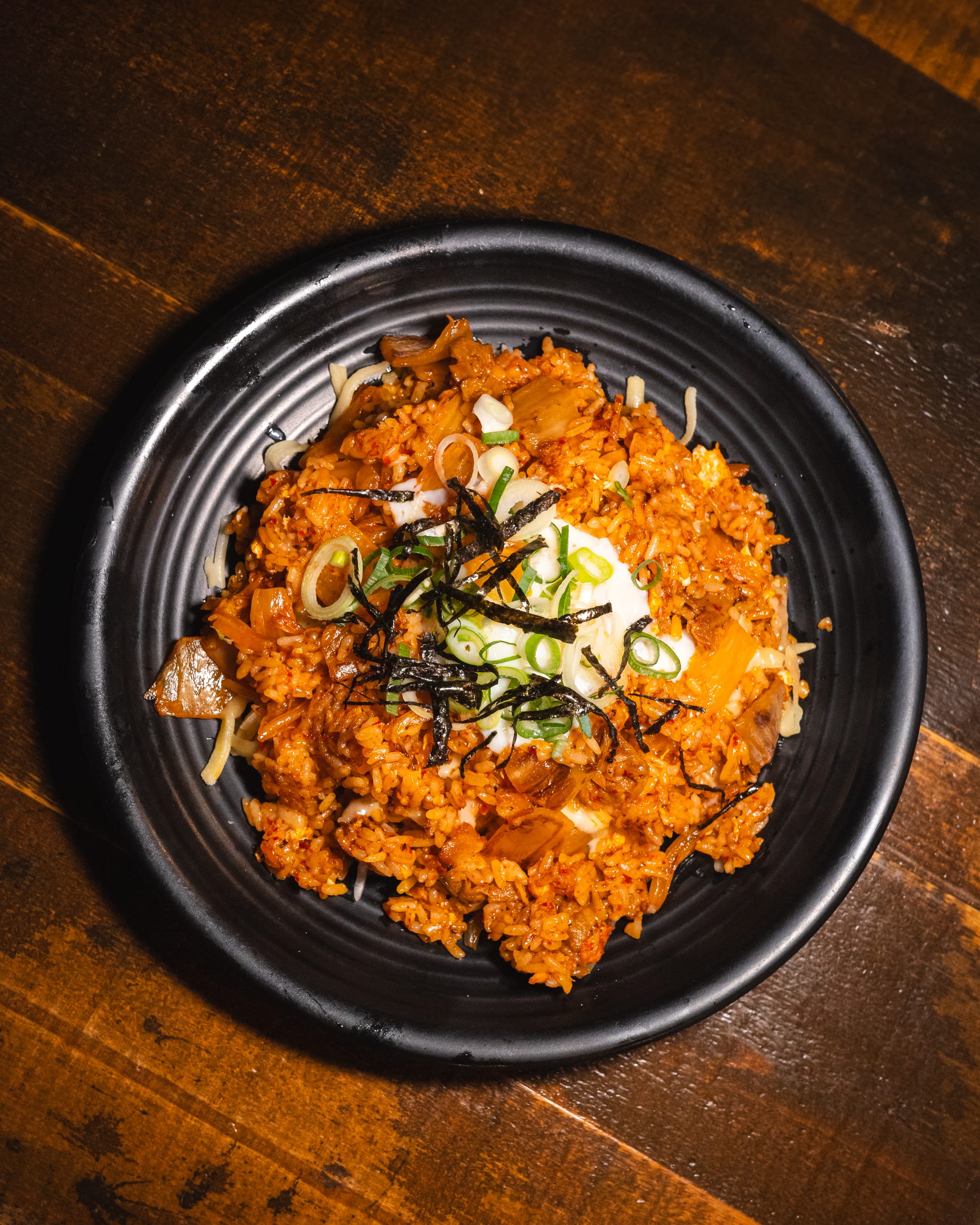 A black bowl filled with spicy kimchi fried rice topped with a fried egg and seaweed strips.