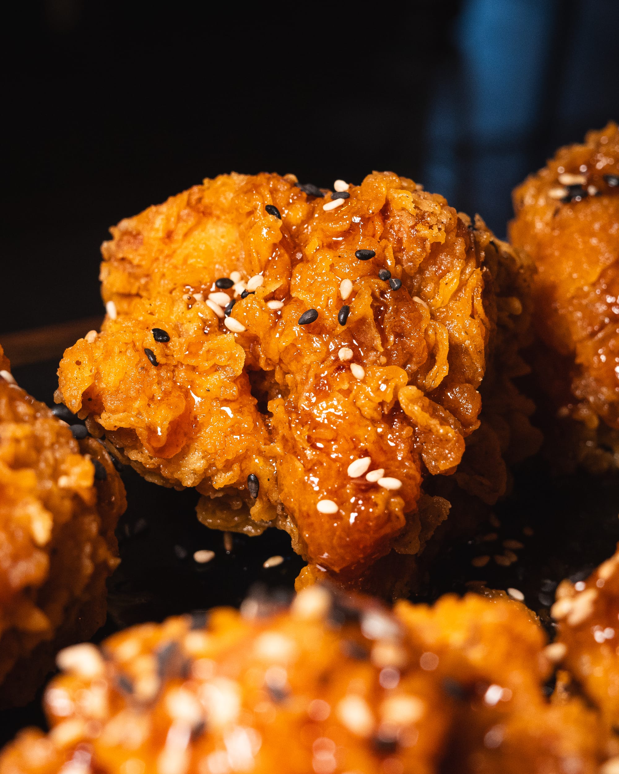 A close-up of crispy, glazed Korean fried chicken sprinkled with sesame seeds.