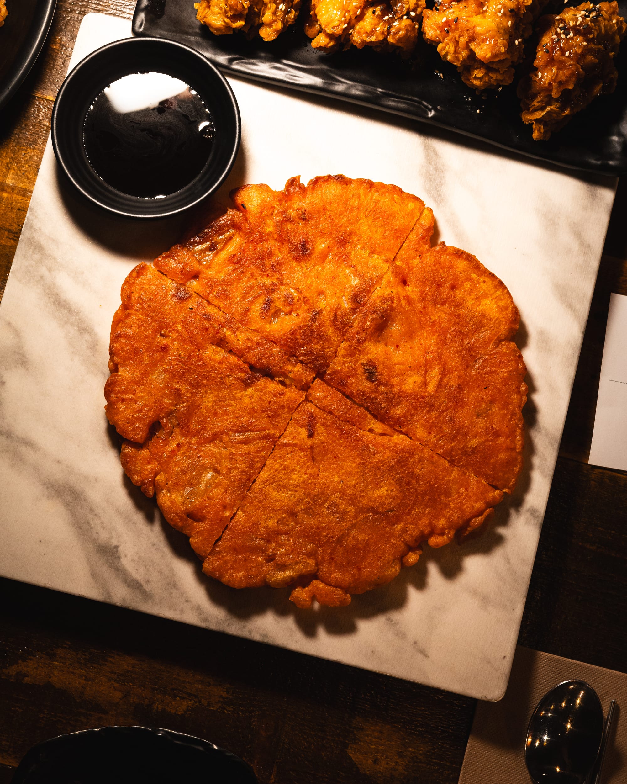 A whole Korean-style fried pancake with a dipping sauce on a black tray.