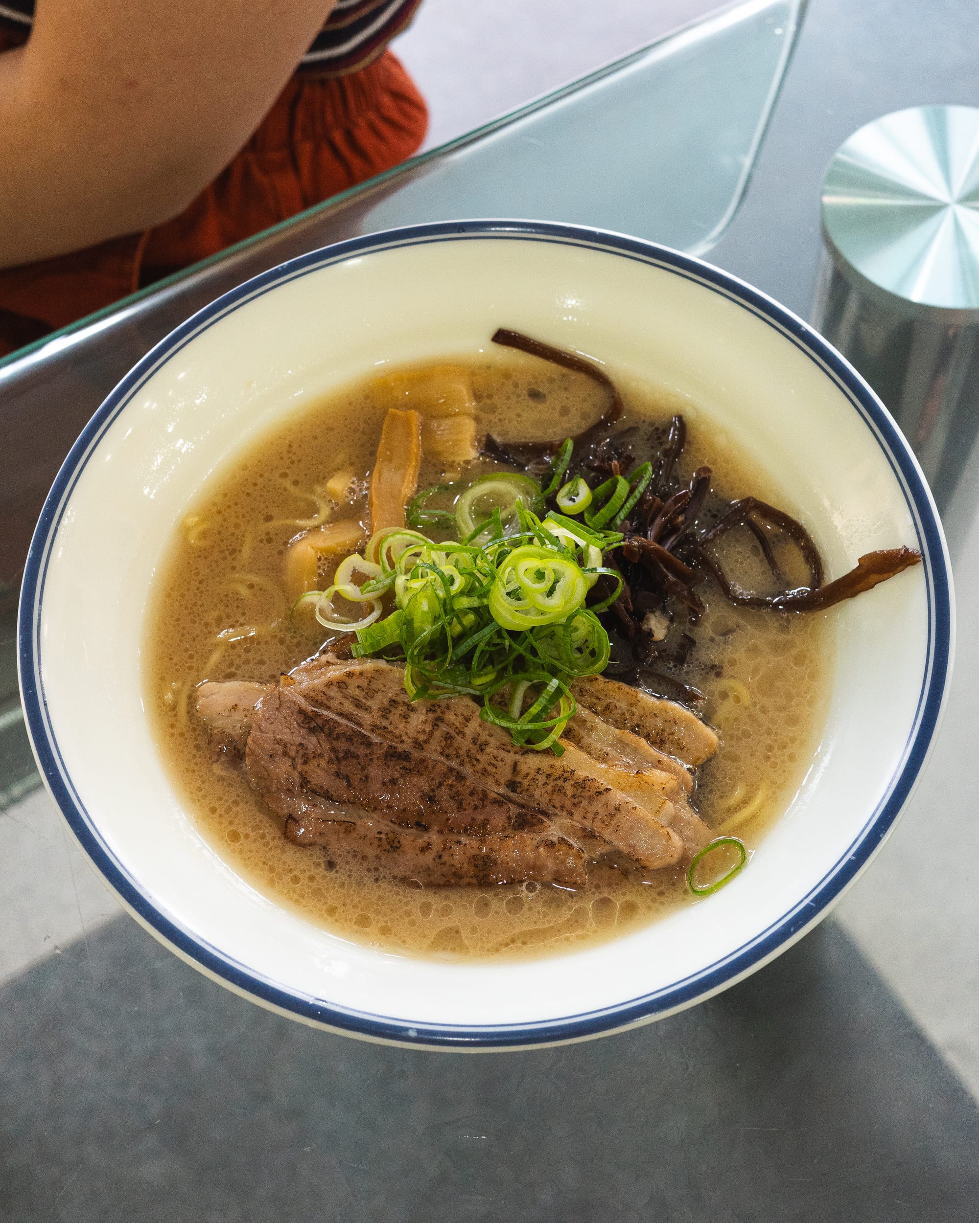 A bowl of ramen with sliced beef, green onions, and mushrooms in a light-colored broth.