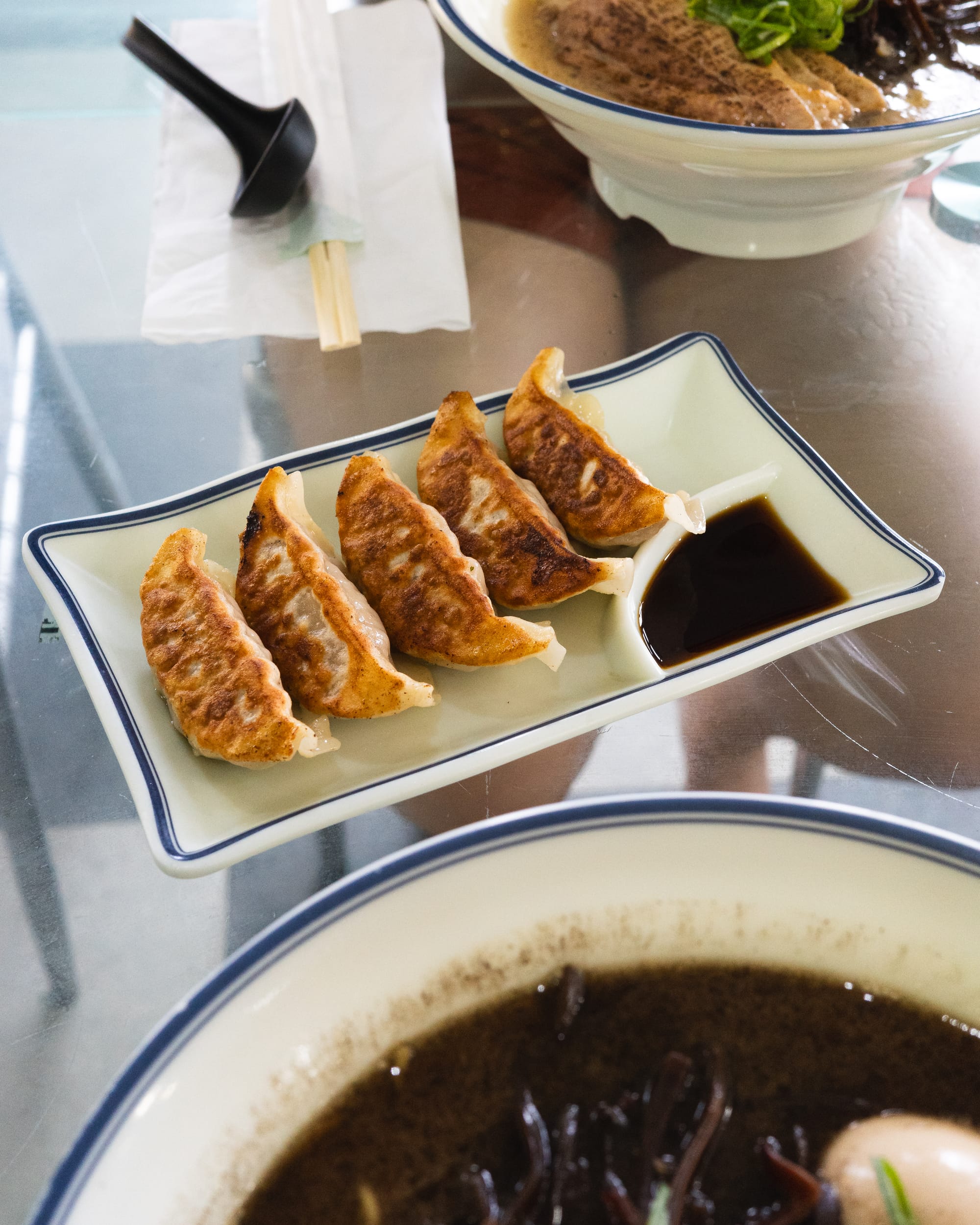 A plate of golden-brown pan-fried gyoza arranged neatly beside a dipping sauce.