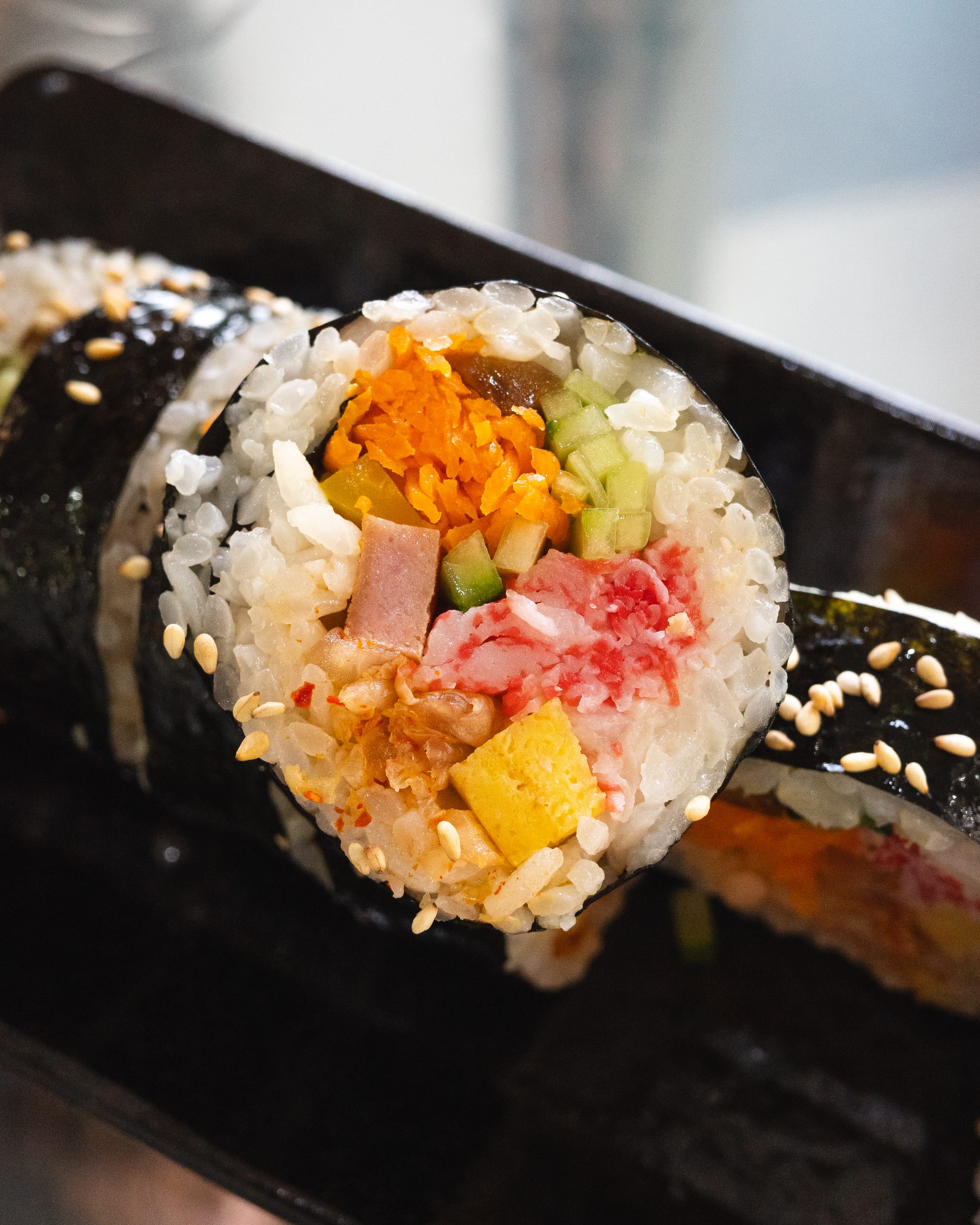 A close-up of a sushi roll wrapped in seaweed, filled with vegetables, seafood, and rice.