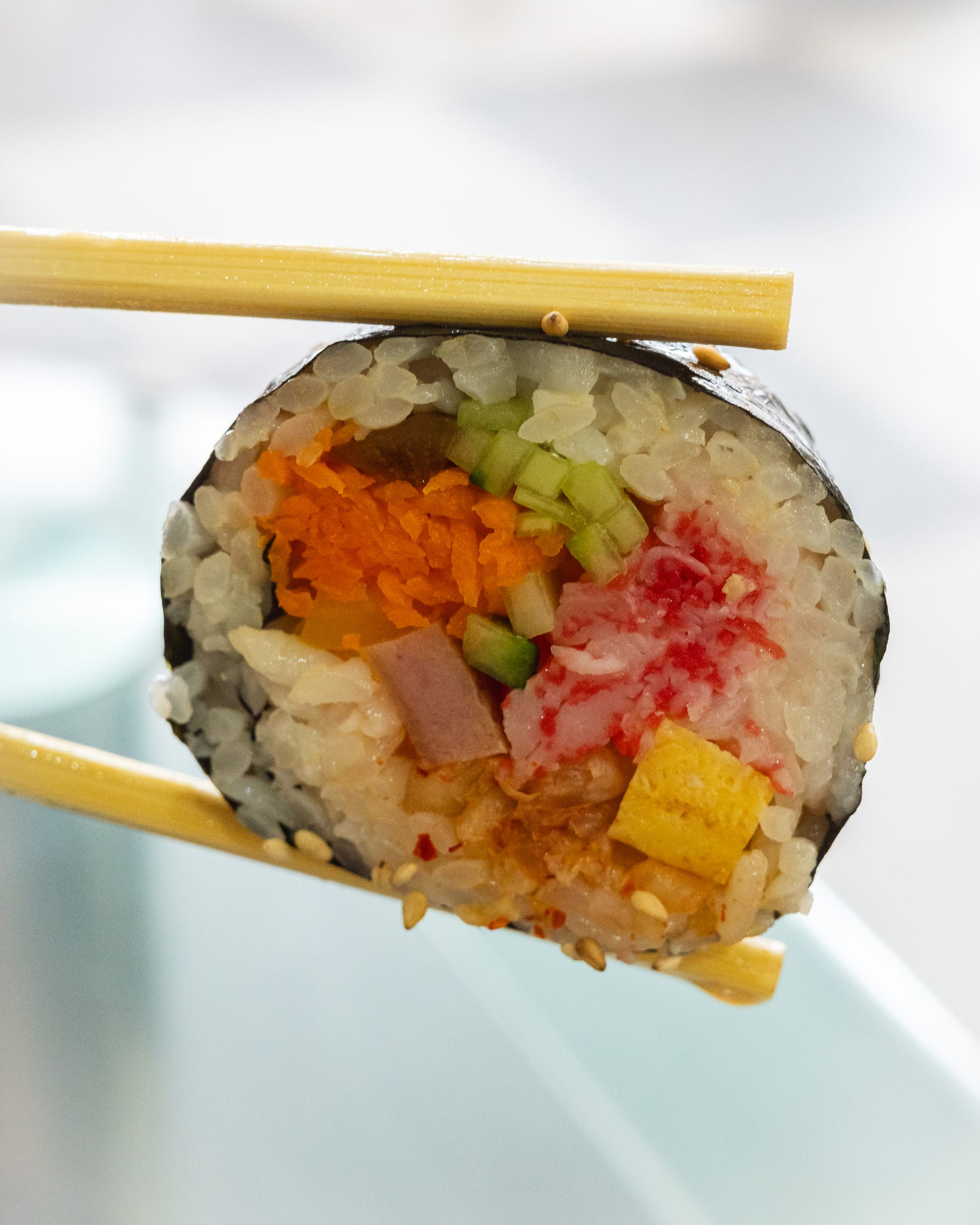 A sushi roll held by chopsticks, showcasing vibrant ingredients like tamago, cucumber, and pickled radish.