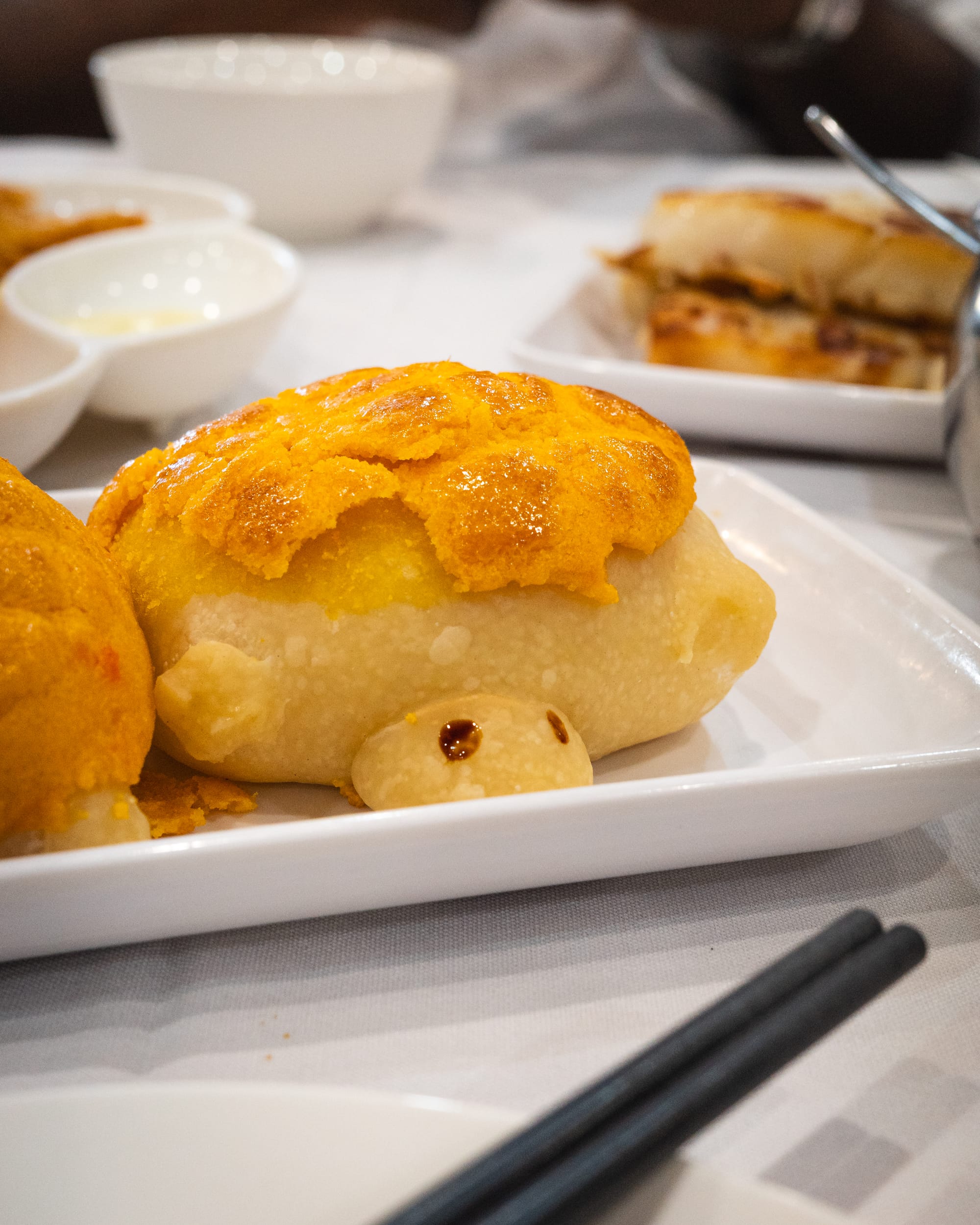 A golden-brown turtle shaped pineapple bun on a white plate, accompanied by chopsticks.