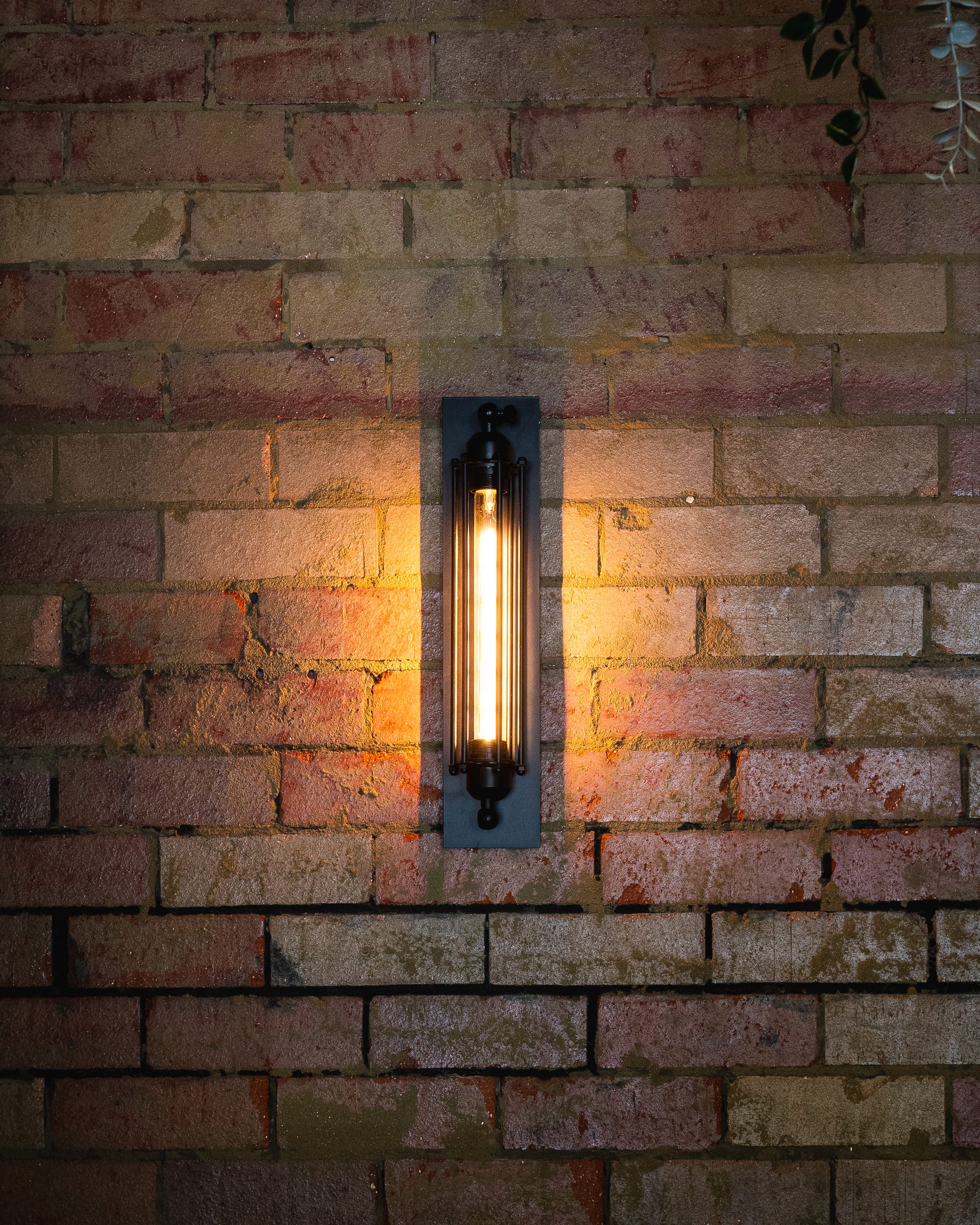 Wall-mounted industrial-style sconce light on an exposed brick wall.