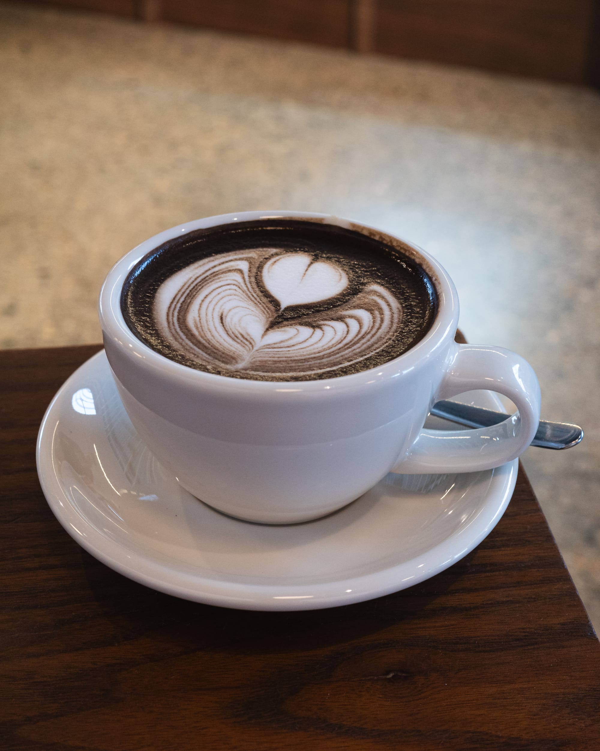 Hojicha latte in a white cup with latte art, placed on a wooden table.