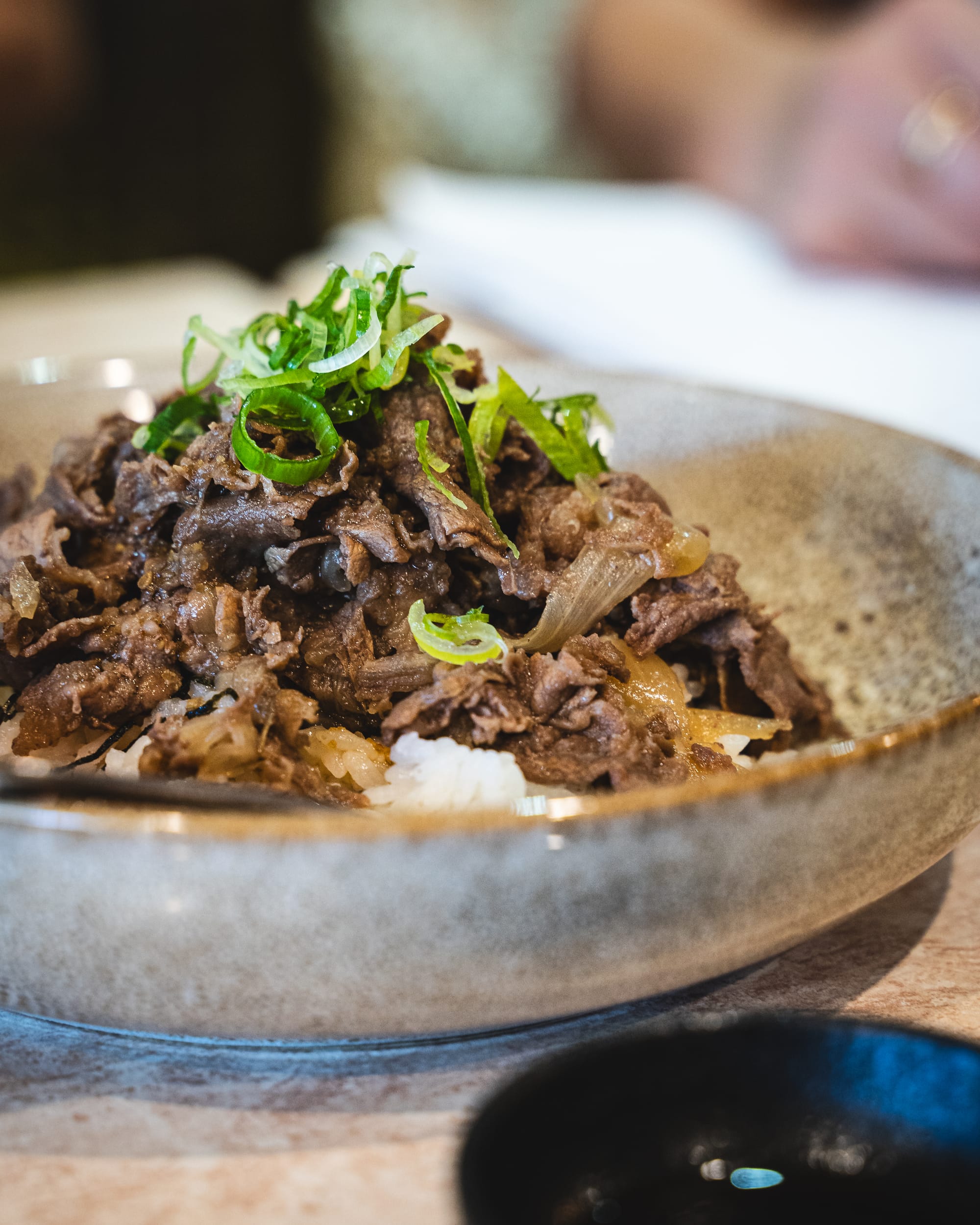 Bowl of braised beef with rice, garnished with chopped green onions.