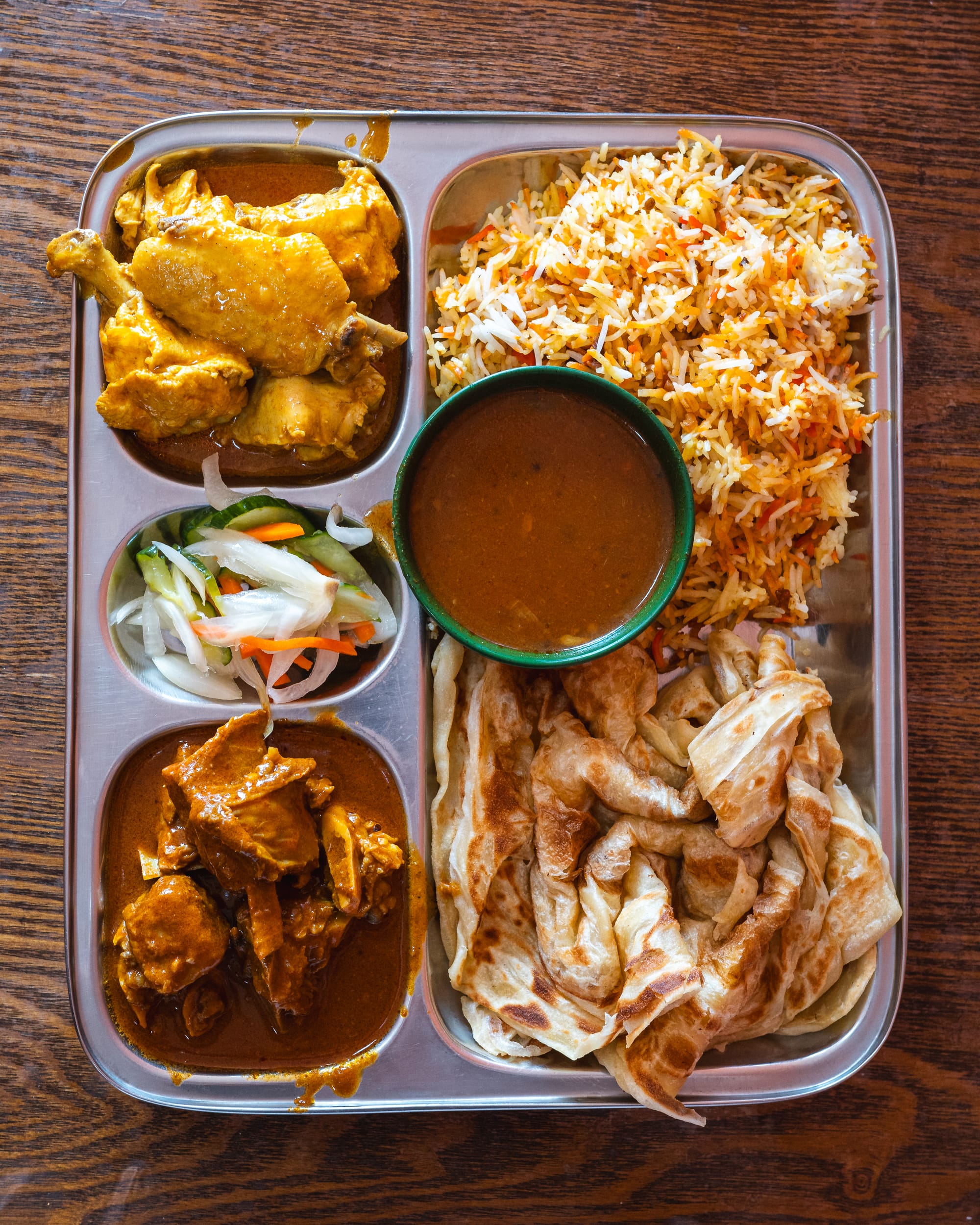 Indian thali with biryani rice, chicken curry, fried chicken, roti, and a small bowl of dhal