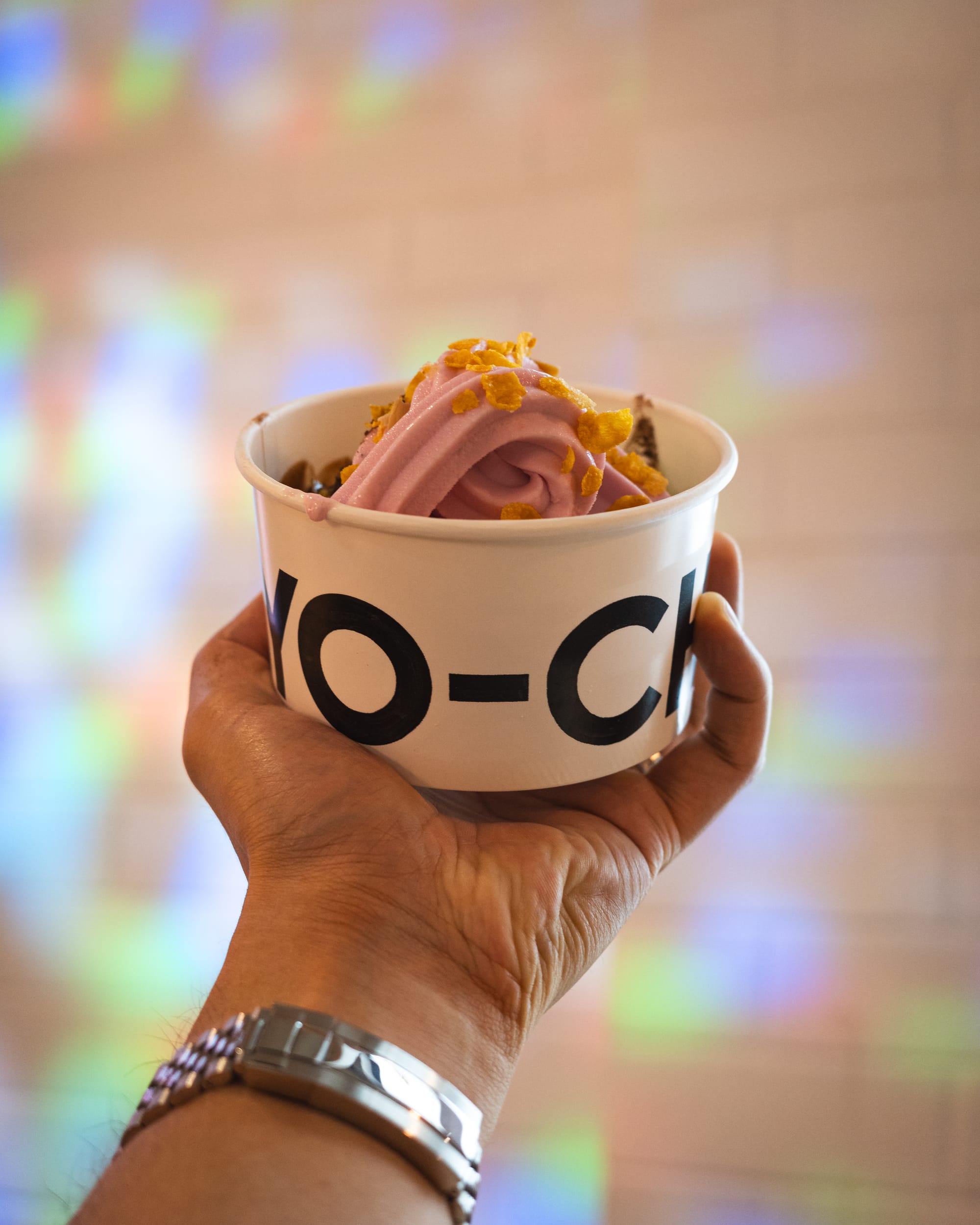 Hand holding a cup of soft serve ice cream in front of a colorful blurred background