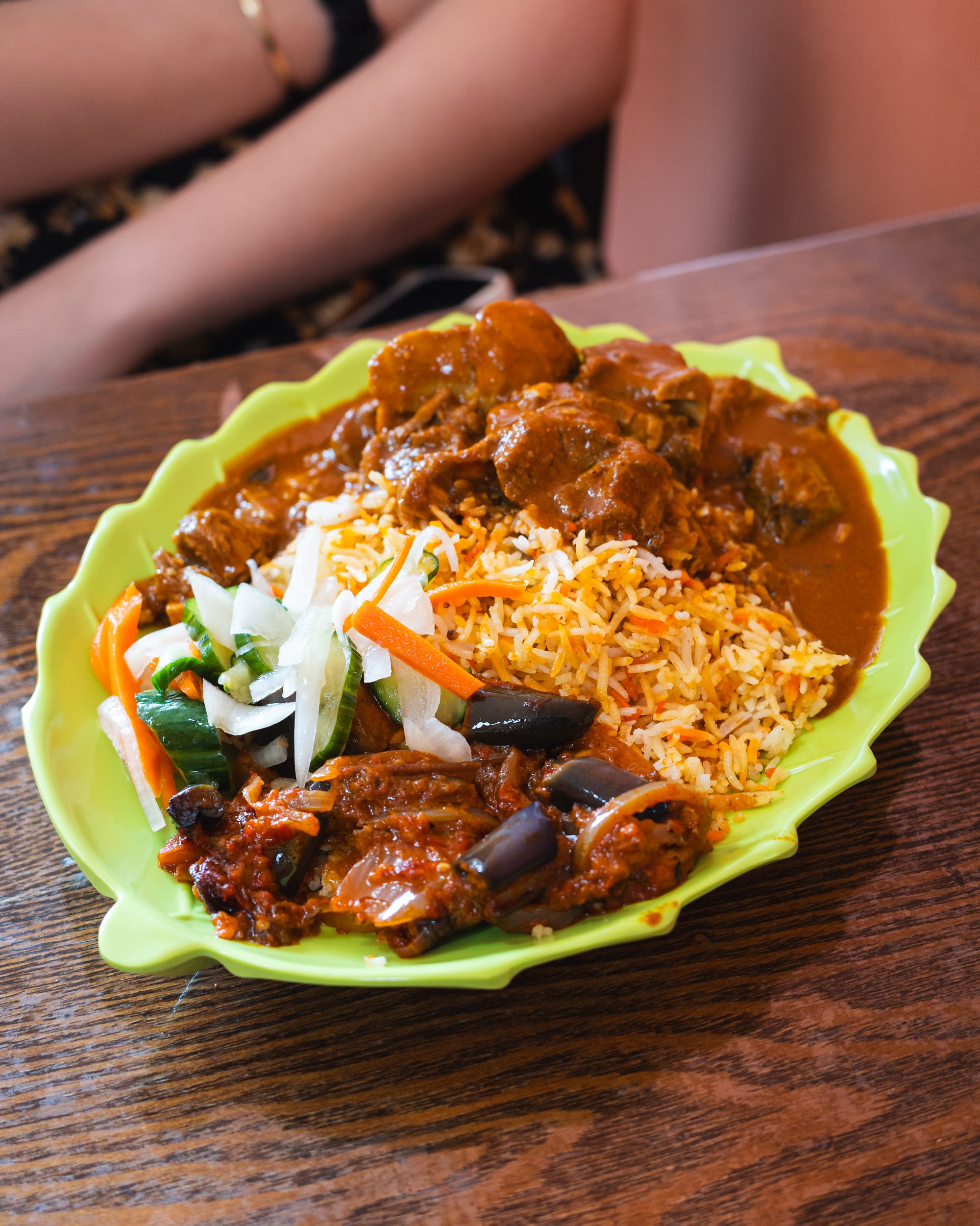 Biryani rice with lamb curry and fresh herbs served on a green plate