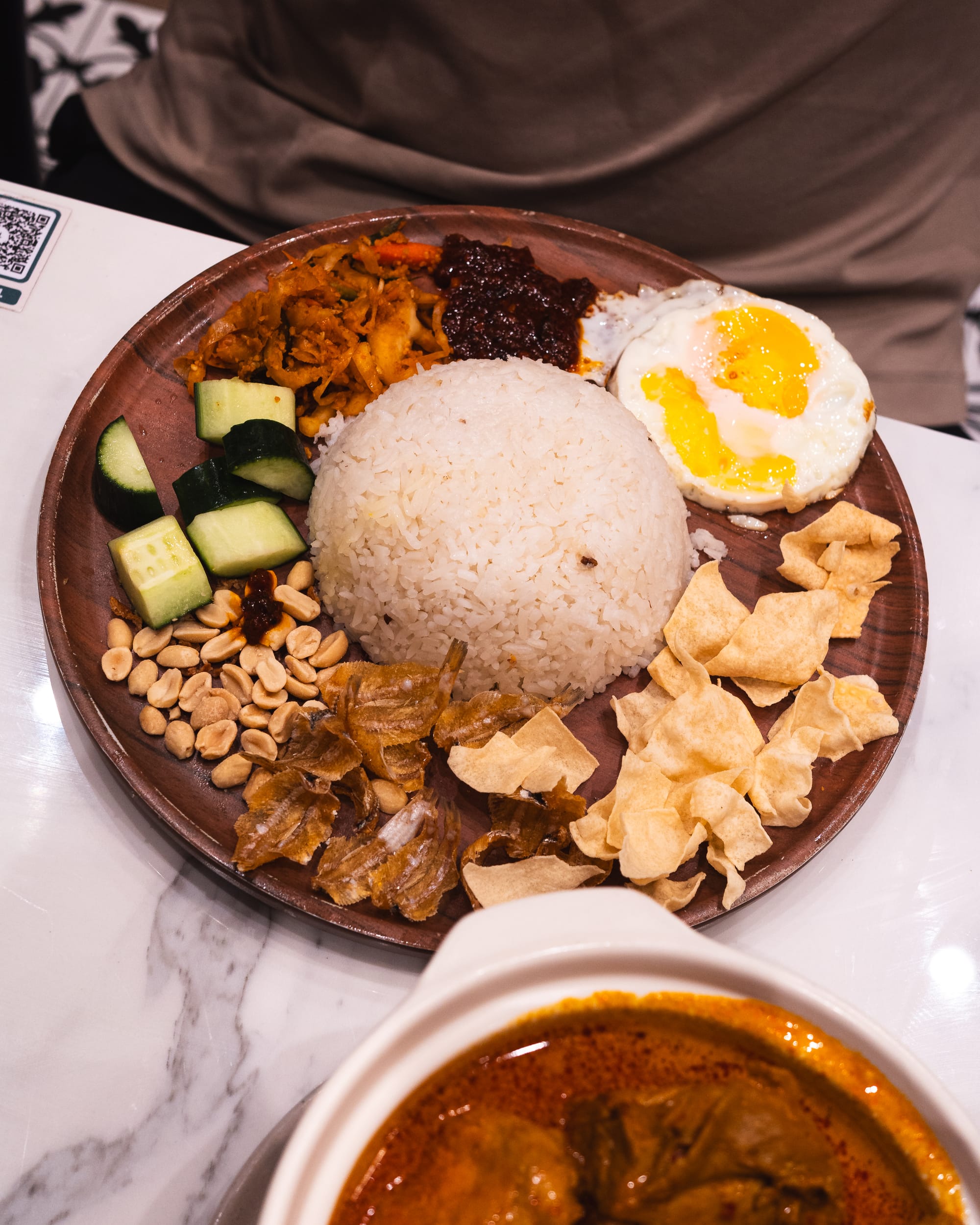 Nasi lemak with sambal, boiled egg, cucumber slices, and rice on a wooden plate