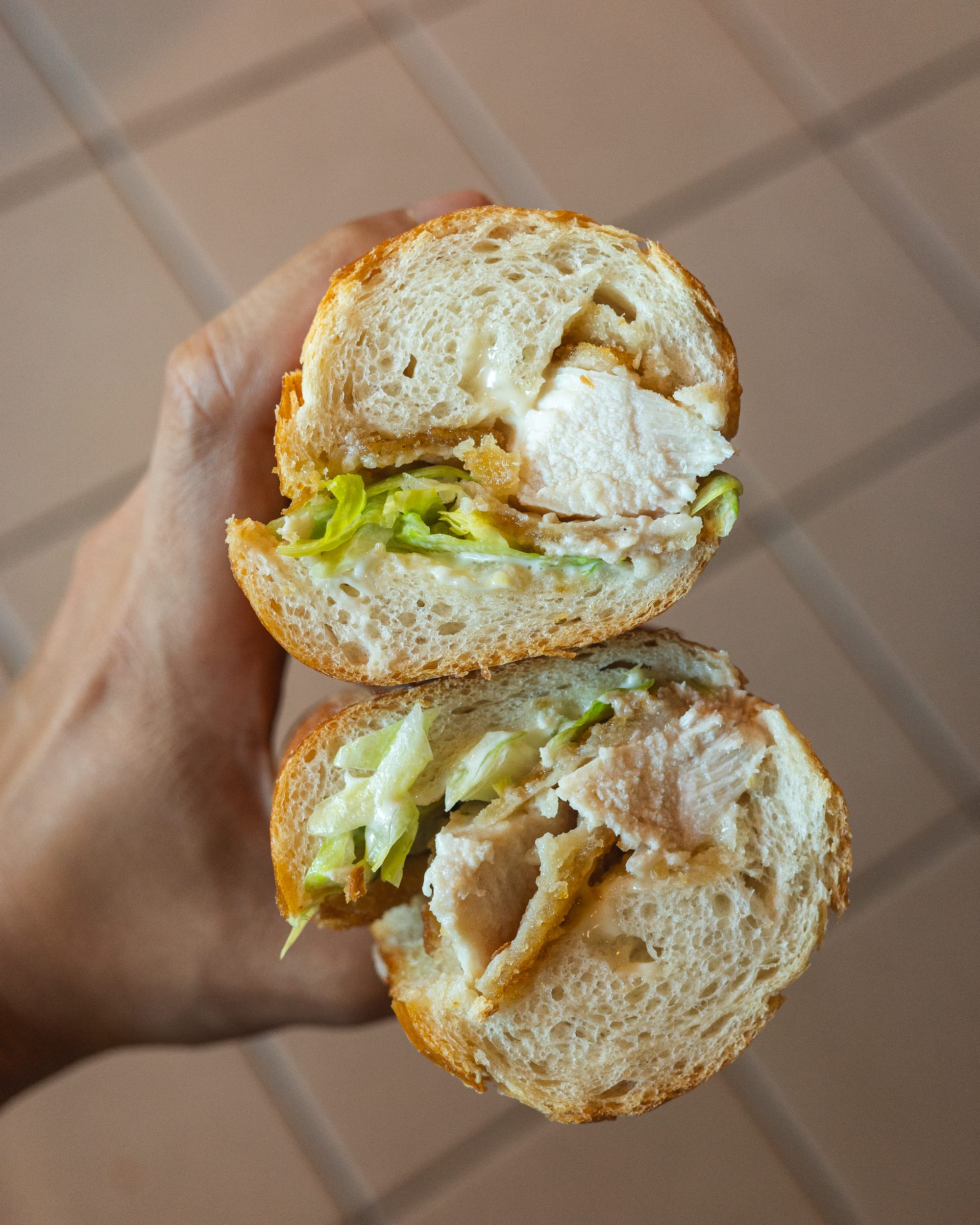 A hand holding a sandwich with lettuce, cheese, and meat, sliced in half.