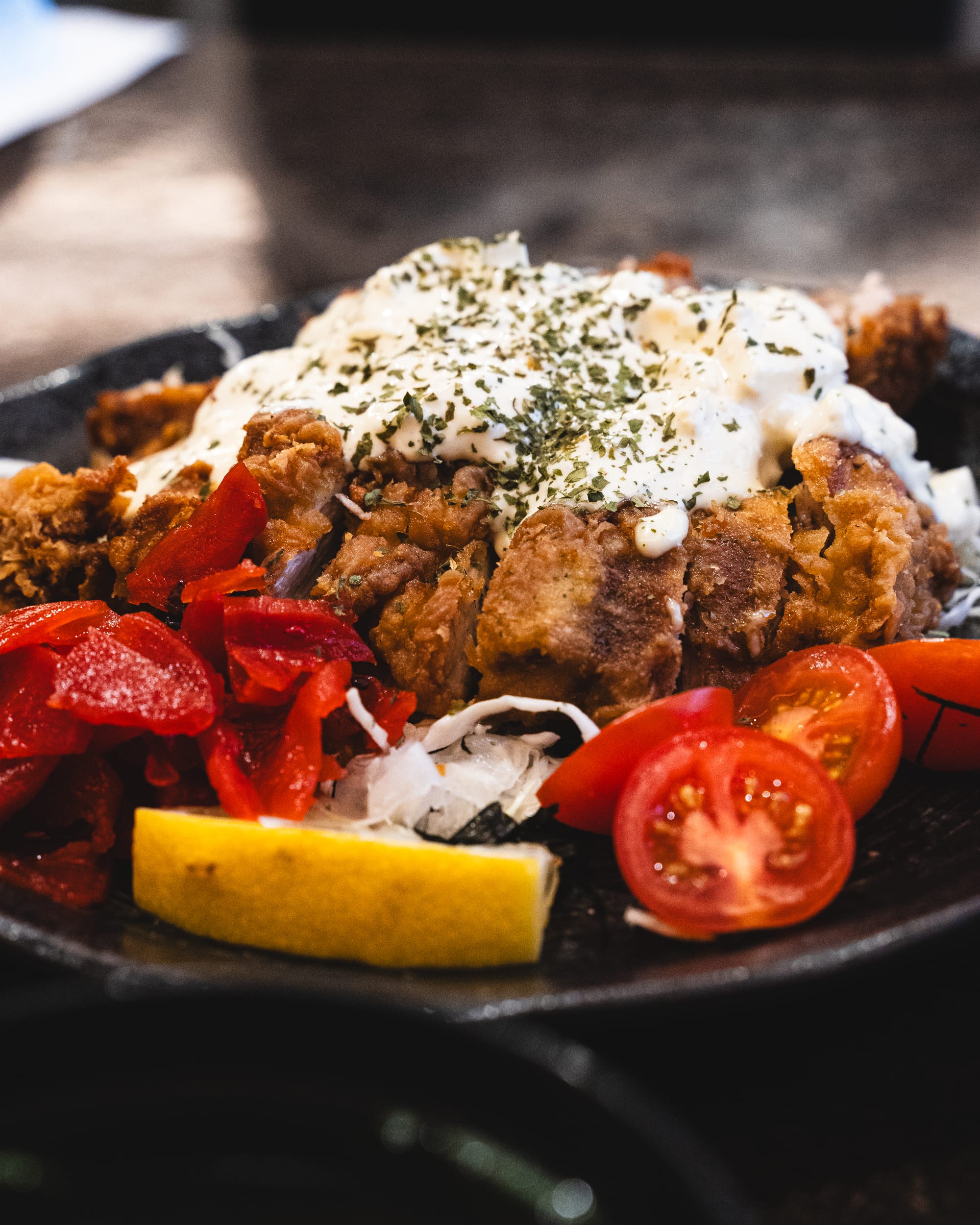 A plate of fried meat with tartare sauce on top top, served with cherry tomatoes.