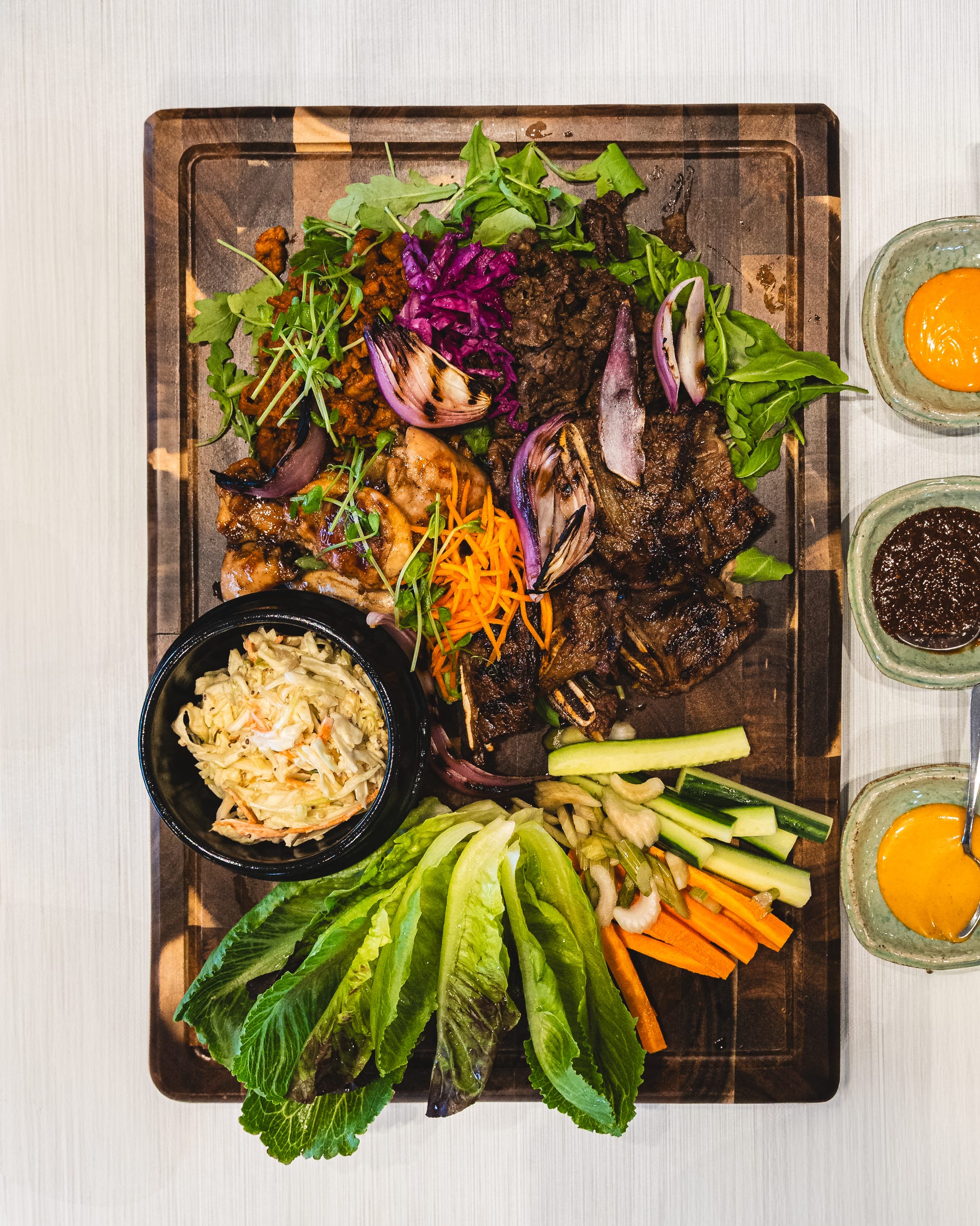 A wooden platter with grilled meats, salad and dipping sauces.