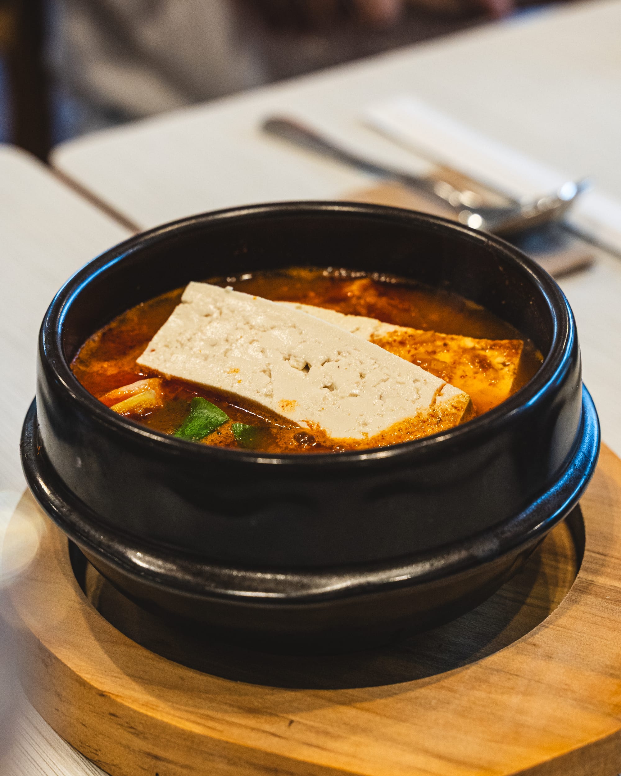 A black stone bowl filled with kimchi and tofu stew, garnished with green onions.