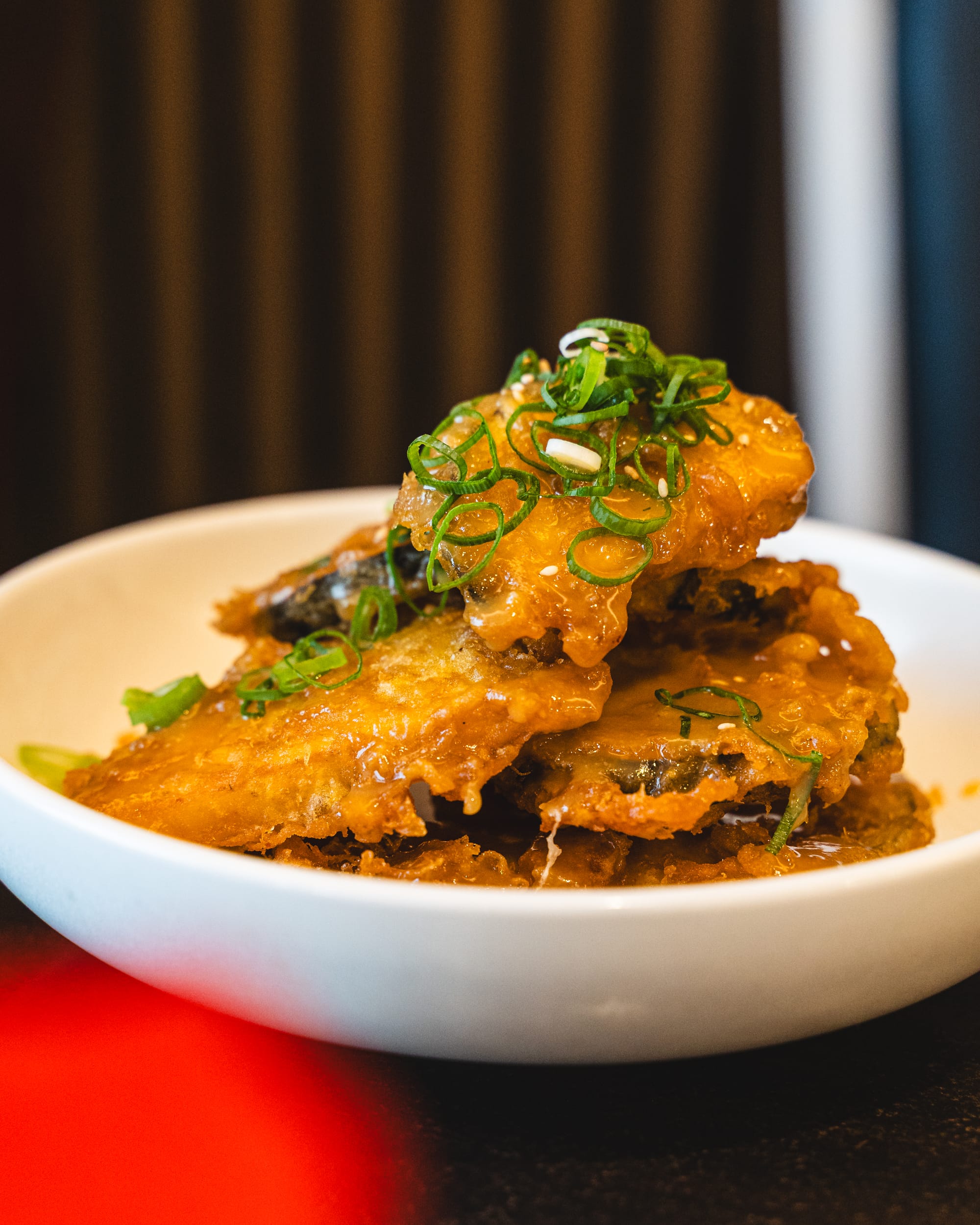 A bowl with golden-brown eggplant tempura stacked on top, garnished with green onions.