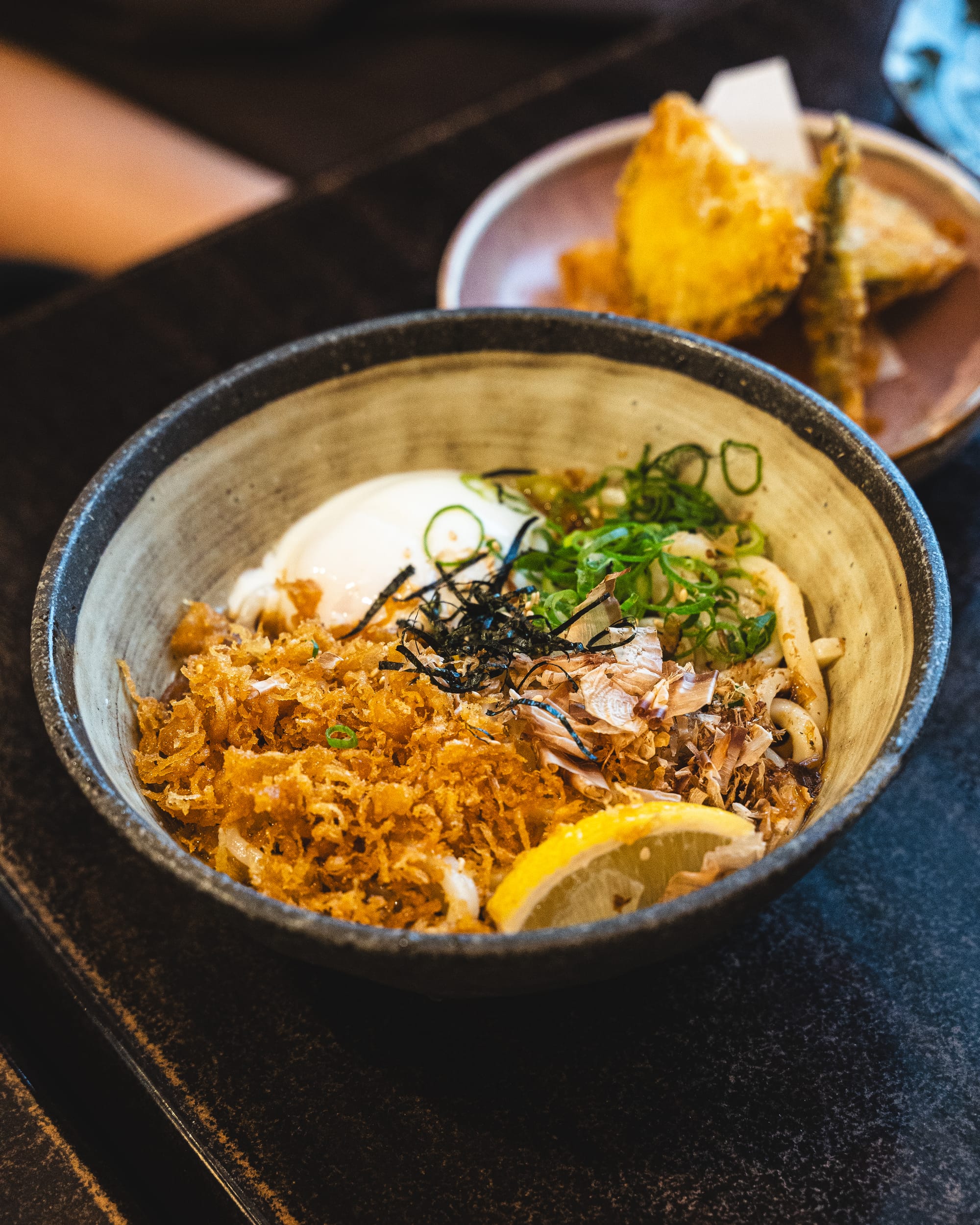 A udon bowl with shredded meat, lemon slices, and a side of crispy topping.