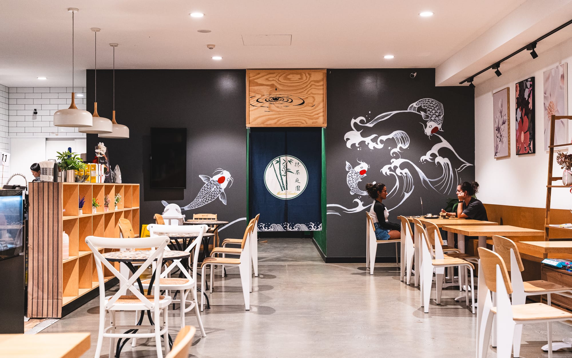 A cozy cafe interior with wooden tables, white chairs, and a blackboard wall featuring artistic chalk designs.