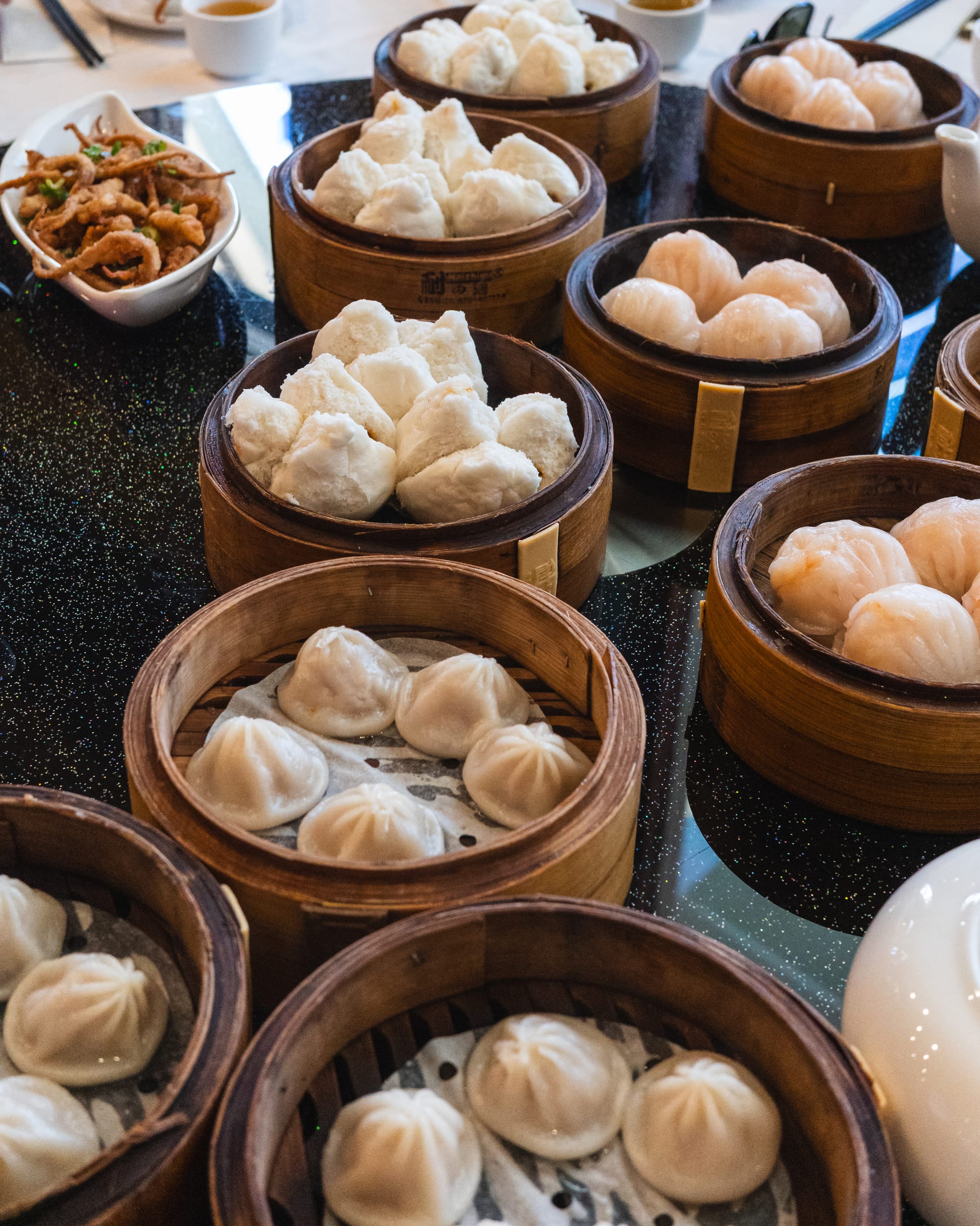 A table filled with bamboo steamers of xiao long bao (soup dumplings), neatly arranged in a restaurant setting.