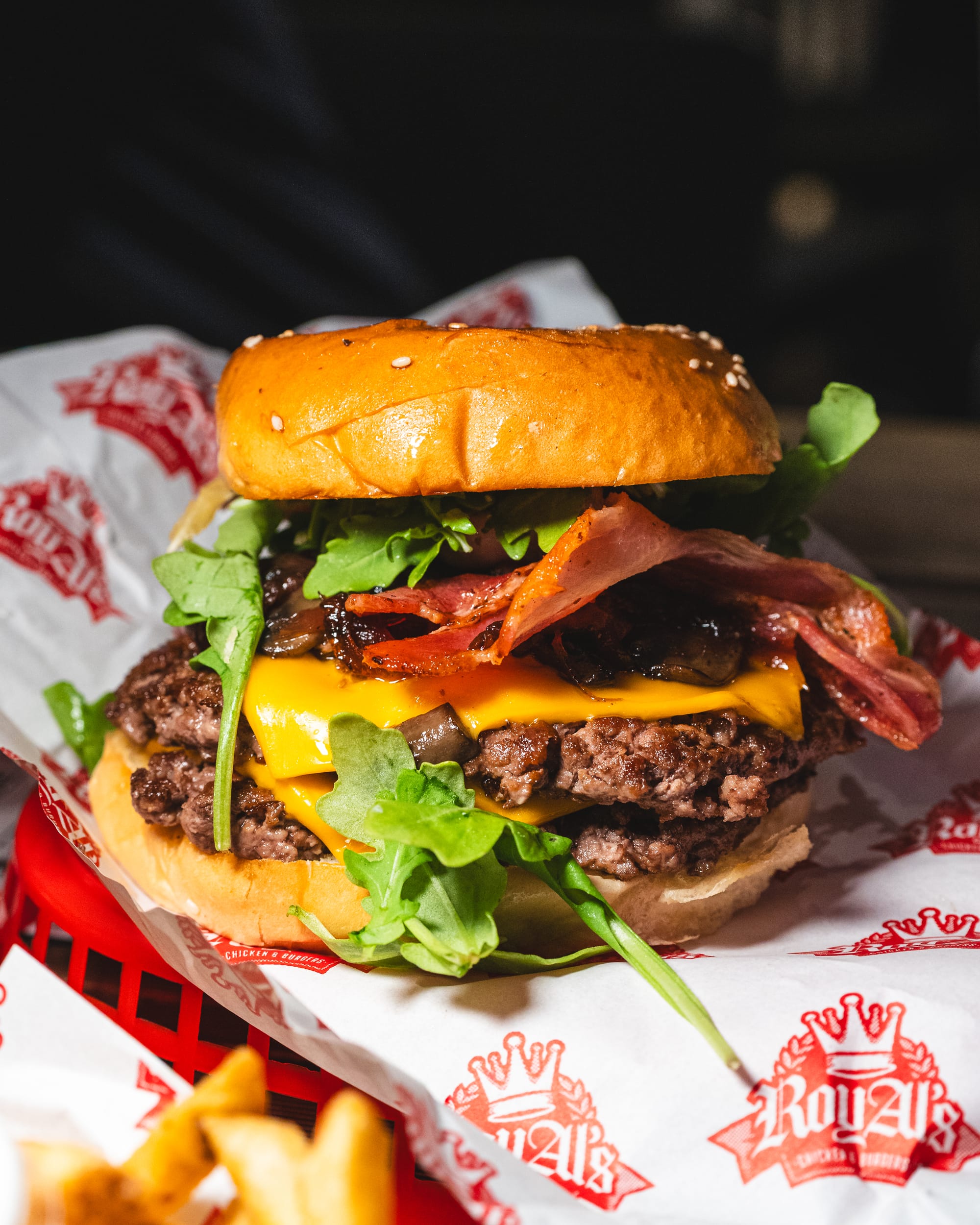 A loaded cheeseburger with crispy bacon, lettuce, and sauce, served with fries in a red basket.