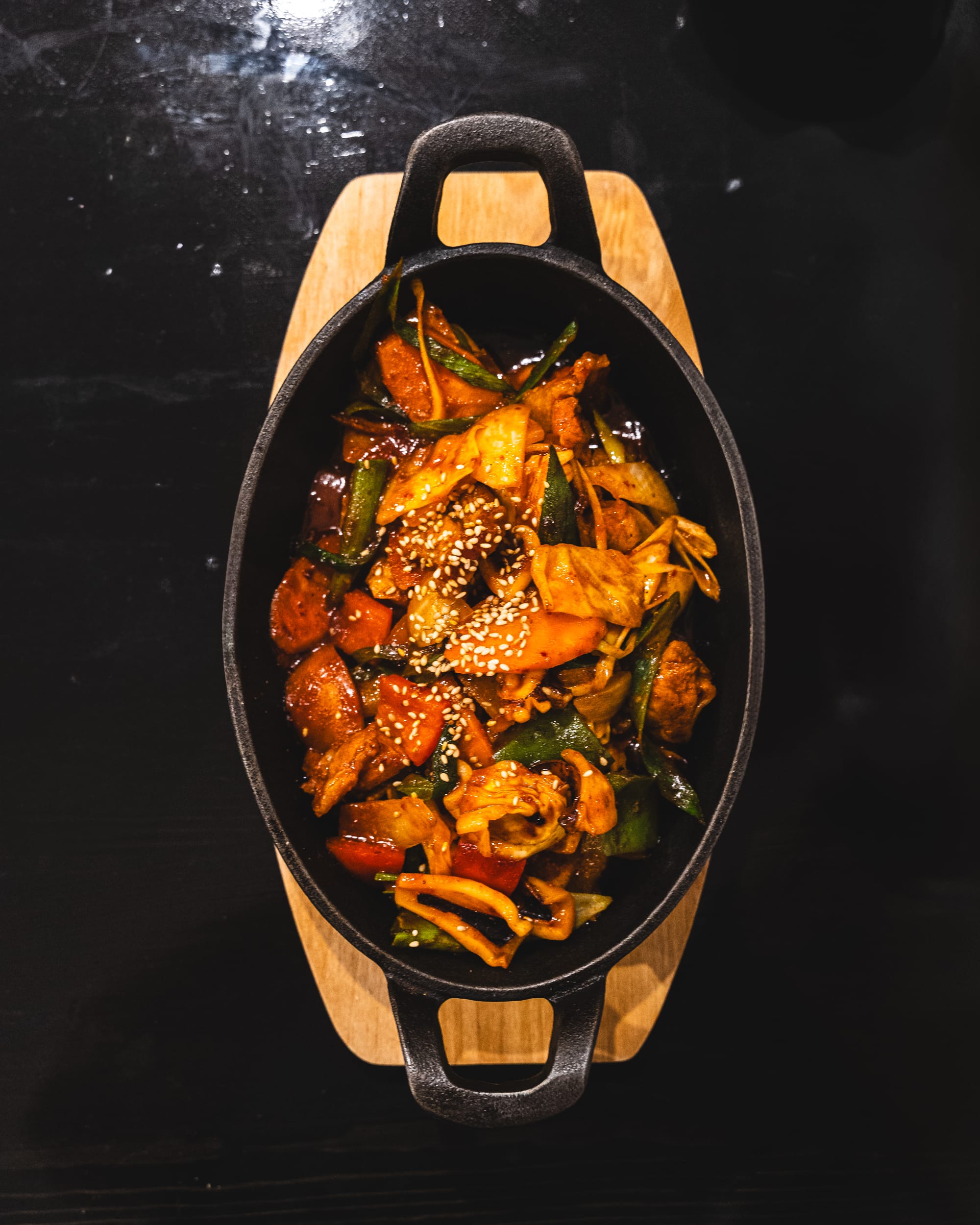 A sizzling hot pot dish with stir-fried meat, vegetables, and chili peppers, served in a black cast iron dish.