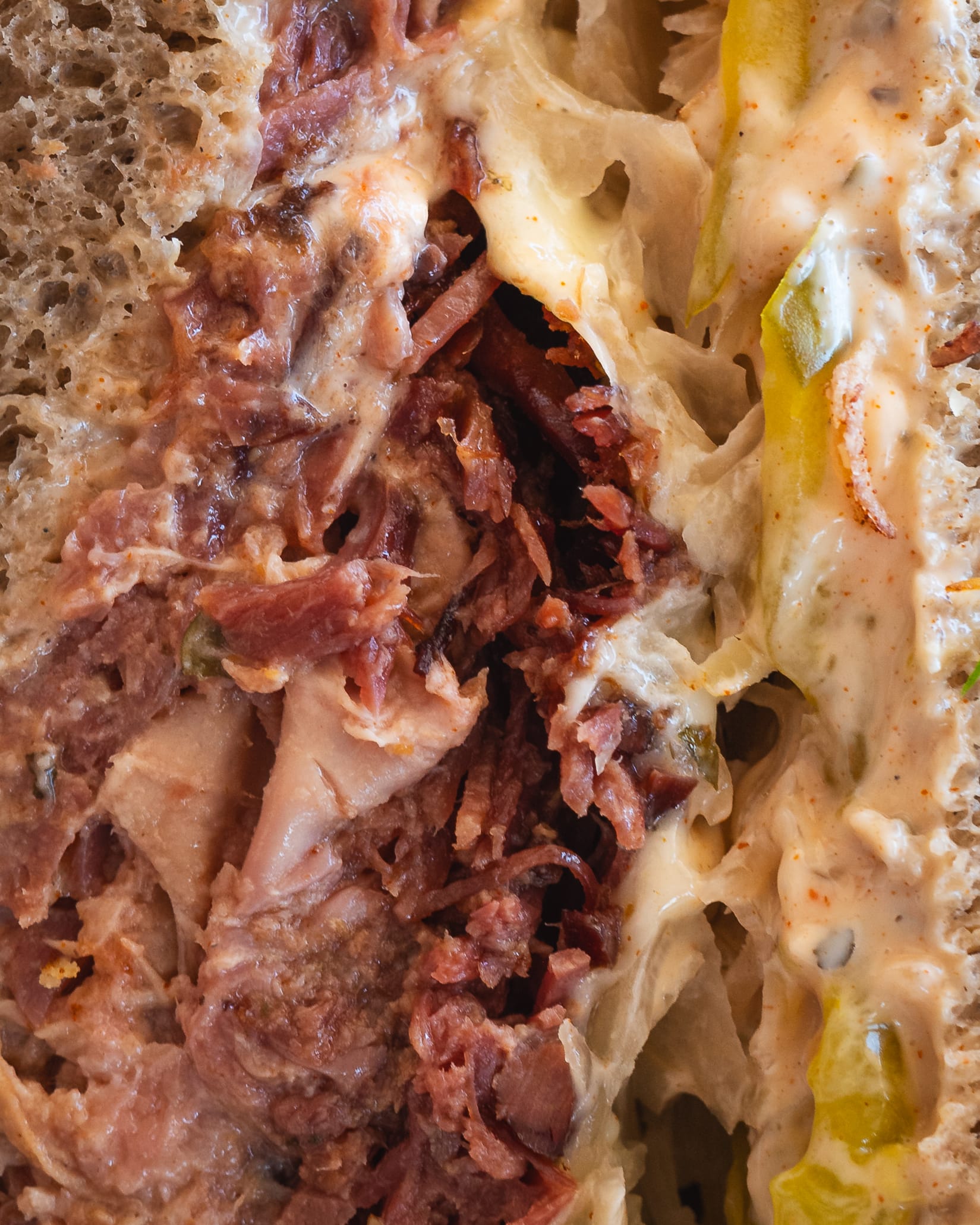 A close-up of a cheesy, saucy sandwich with shredded meat and melted cheese.