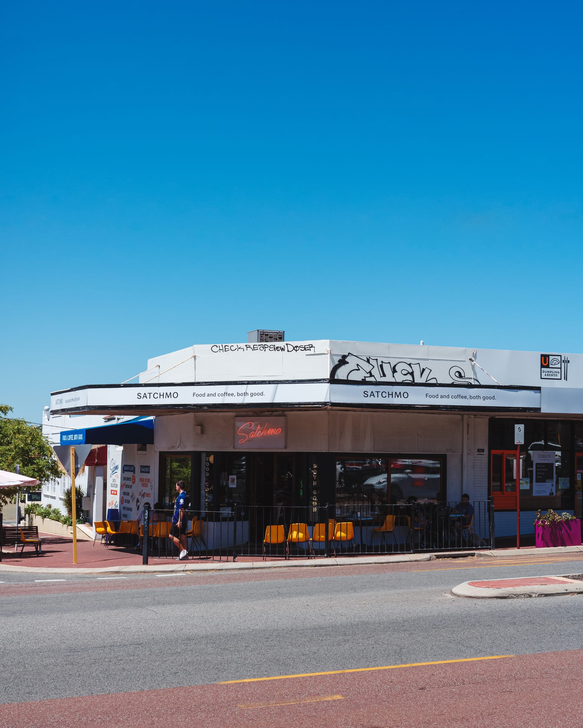 An exterior shot of a café with outdoor seating, a blue sky in the background.