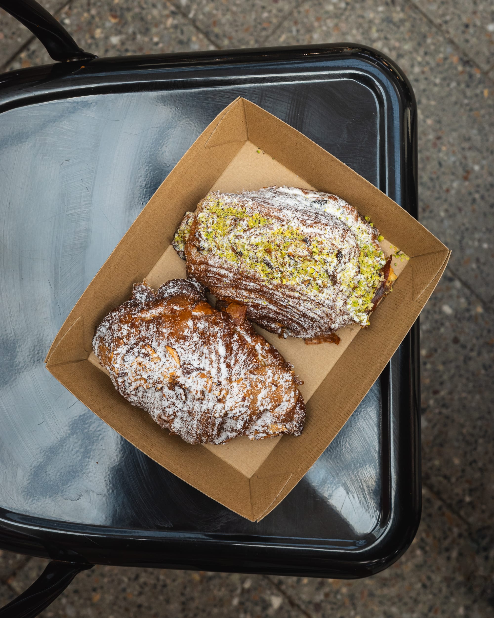 A tray with a pastry dusted in powdered sugar and a sandwich with green filling, served on a metal chair.